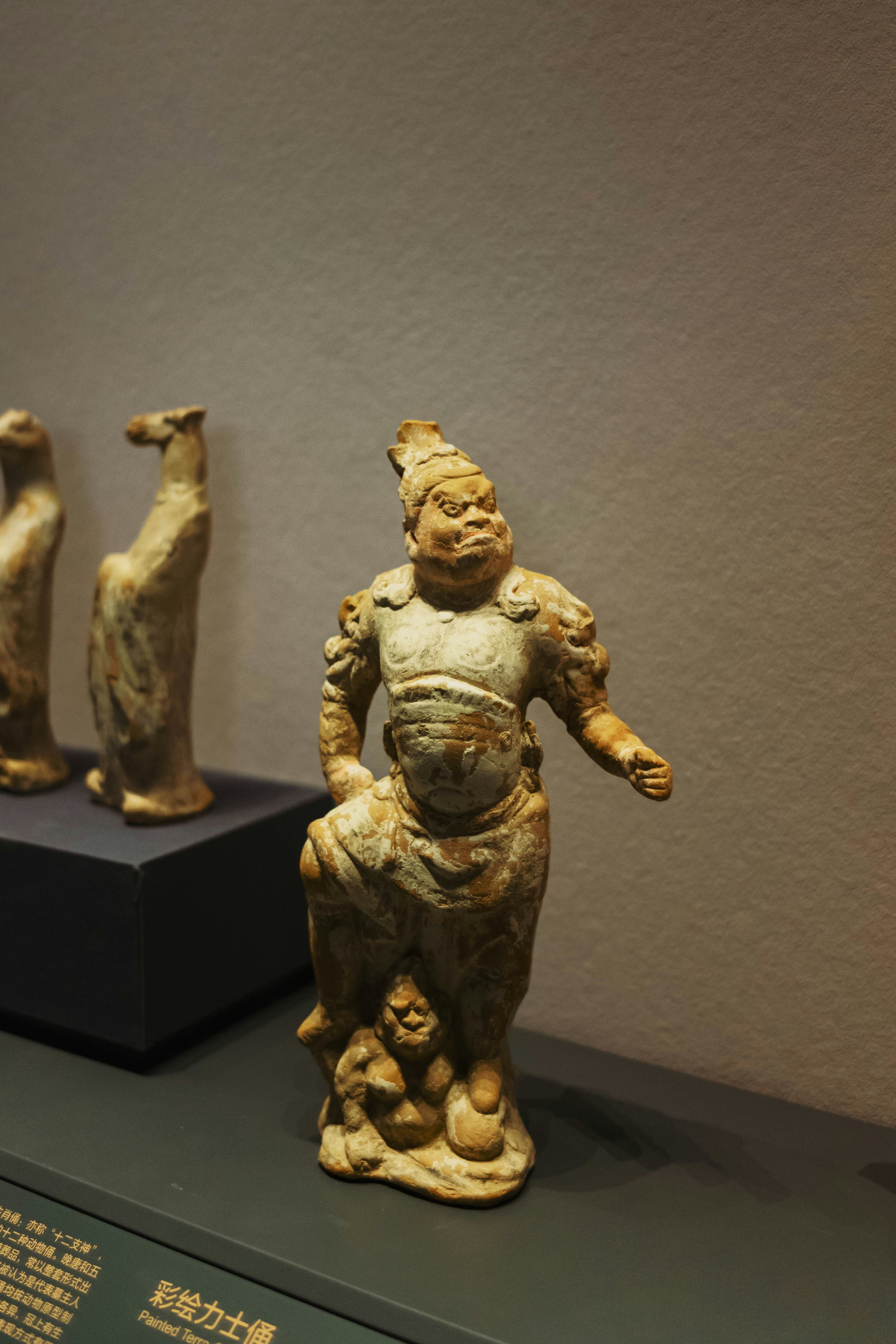 A painted terracotta warrior figurine standing on a small creature in a museum display