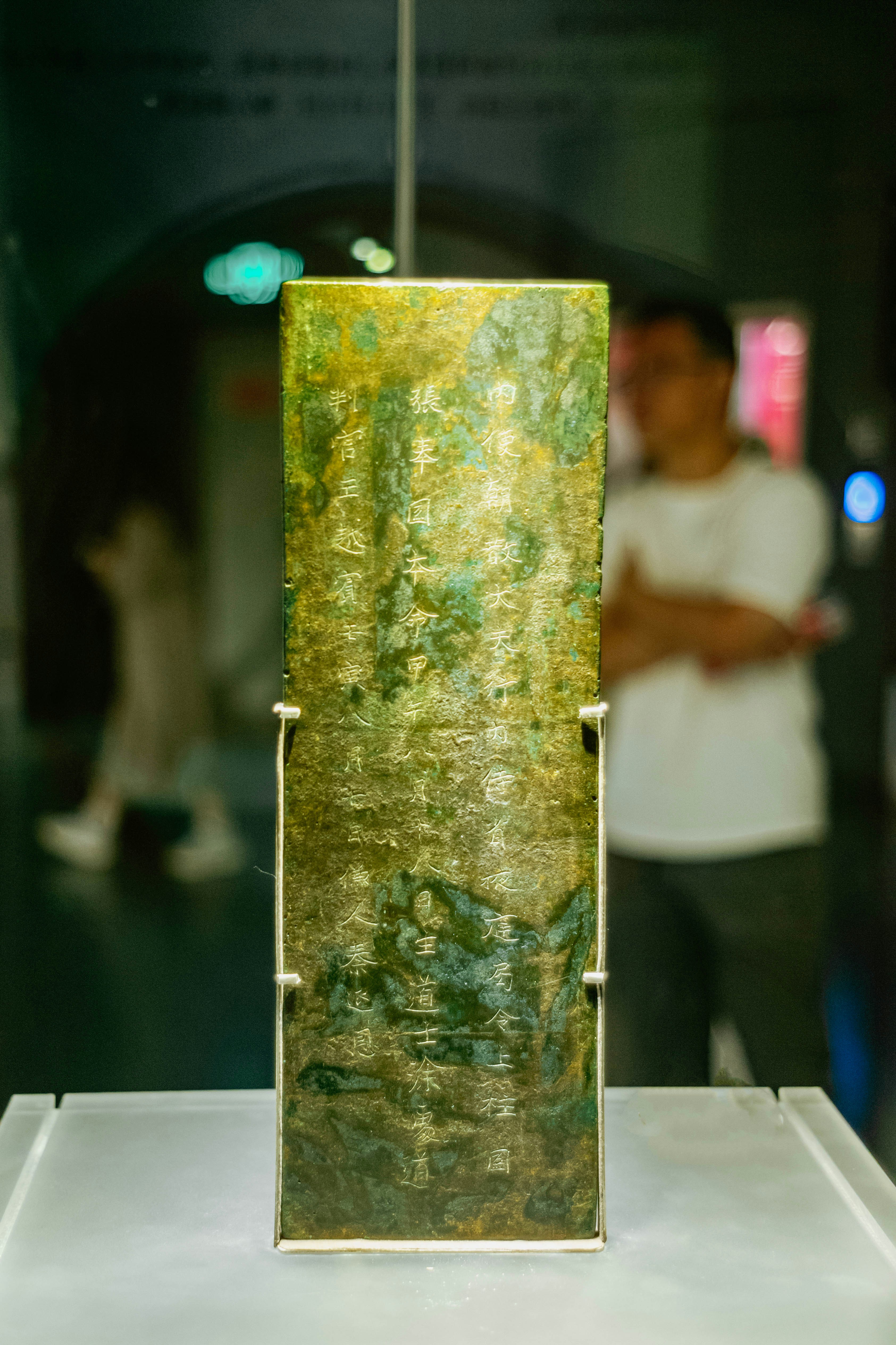 An ancient rectangular bronze plaque with engraved Chinese characters on a display stand