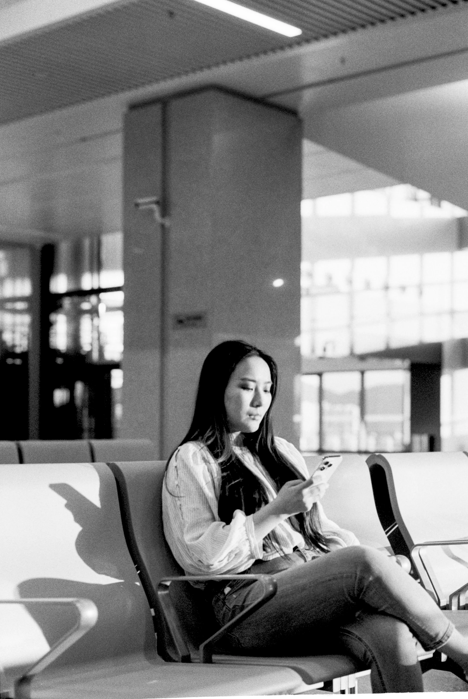A traveler using a smartphone while waiting in a bright airport terminal