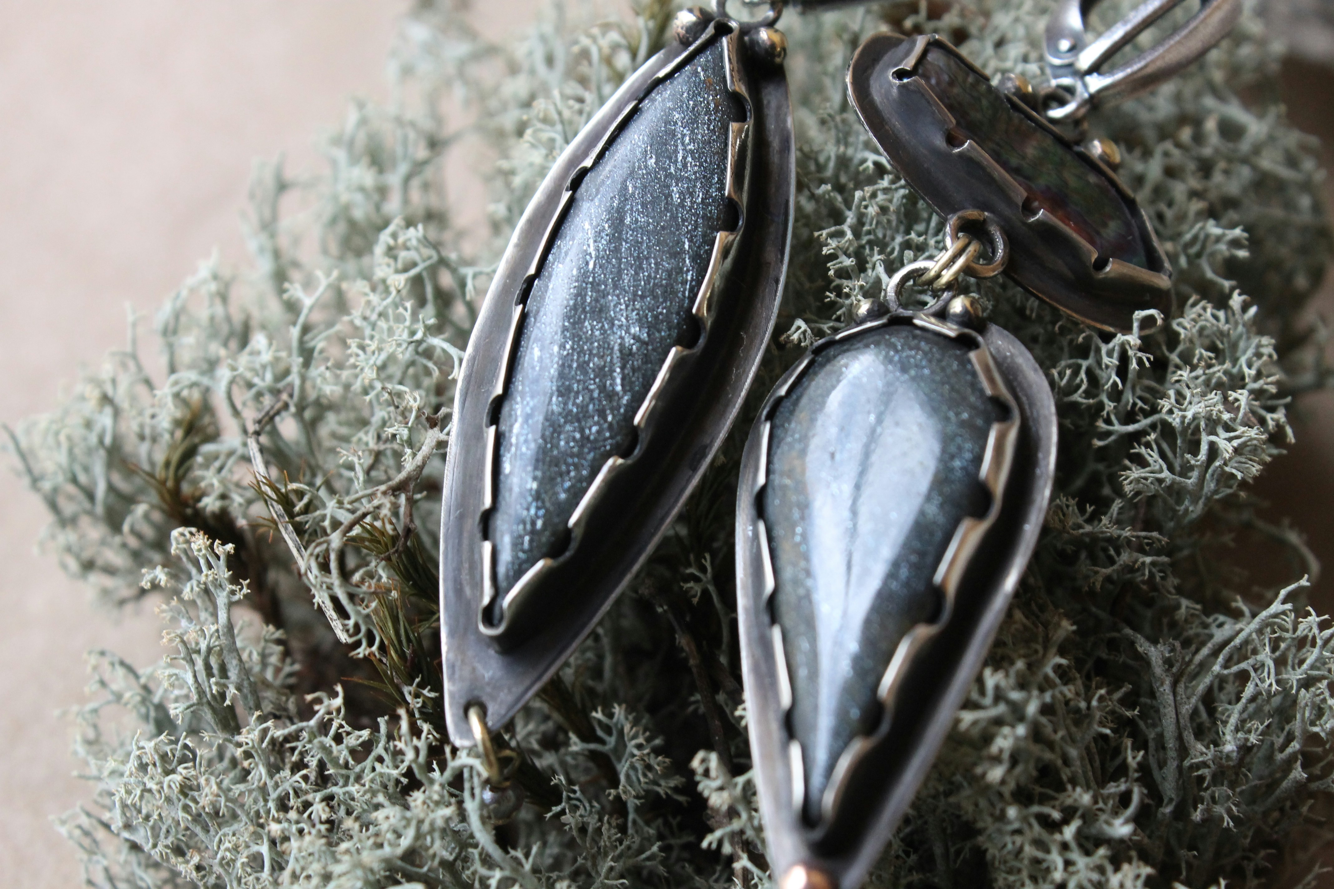 Deux boucles d’oreilles en argent avec des pierres gris foncé reposant sur un lit de lichen