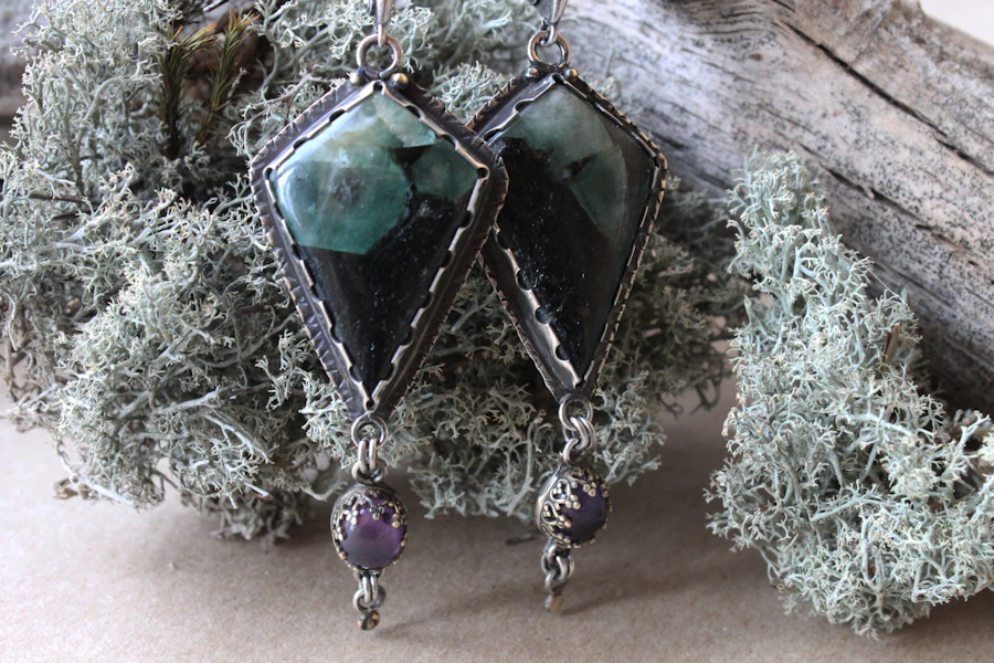 Pendientes de plata en forma de cometa con piedras verdes y negras sobre liquen