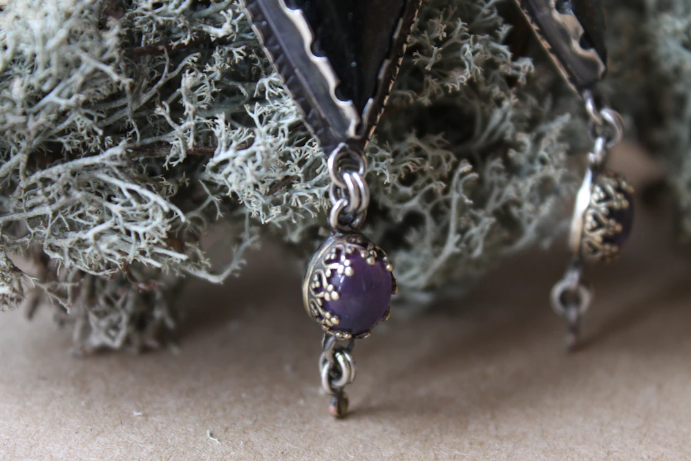 Amethyst drop earrings hanging against natural moss