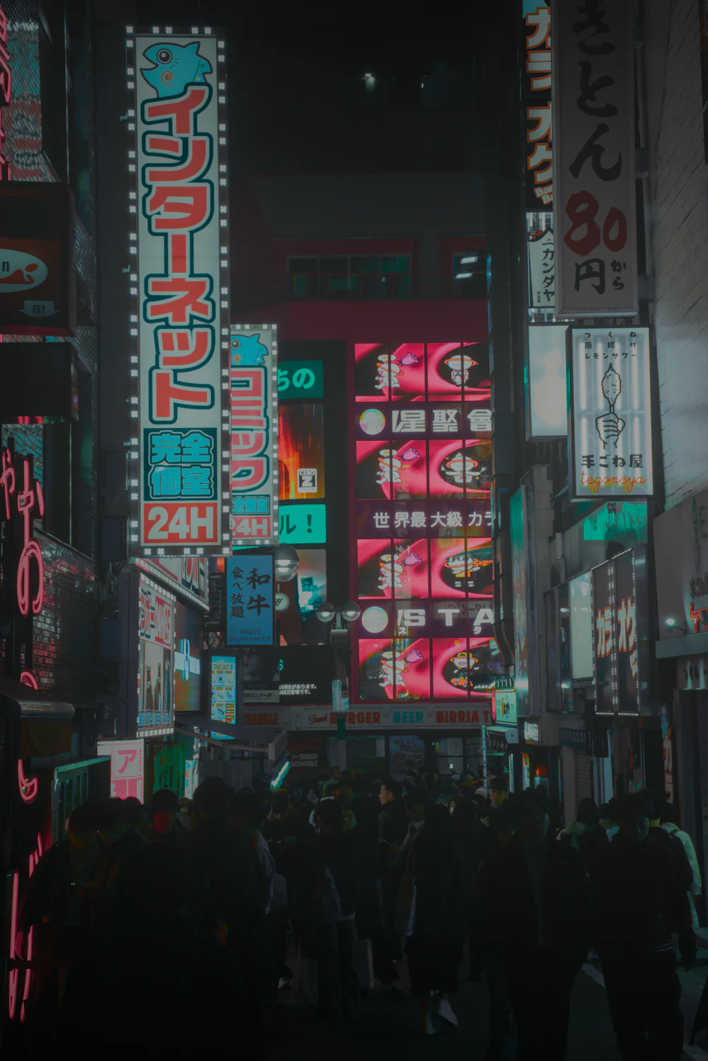 A narrow street at night lined with glowing neon signs.
