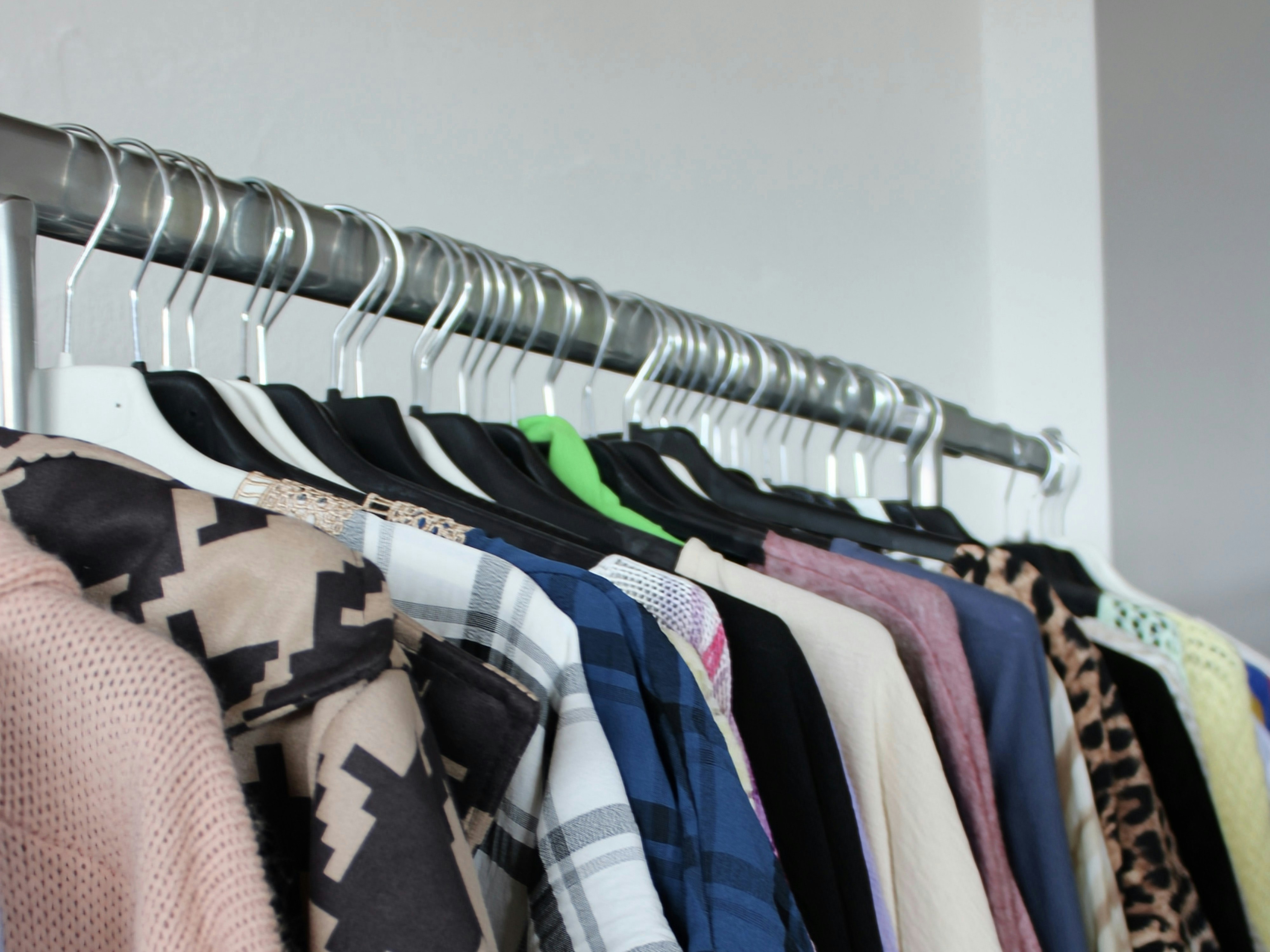 A row of assorted garments hanging on a metal rack against a white wall