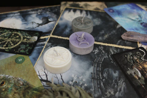 Three small wax candles with embossed symbols on a surface of illustrated tarot cards