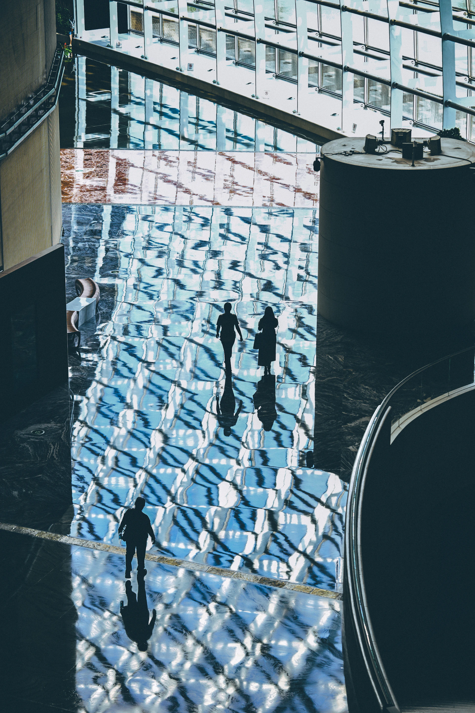 Three people in silhouette walking across a polished floor reflecting a glass ceiling