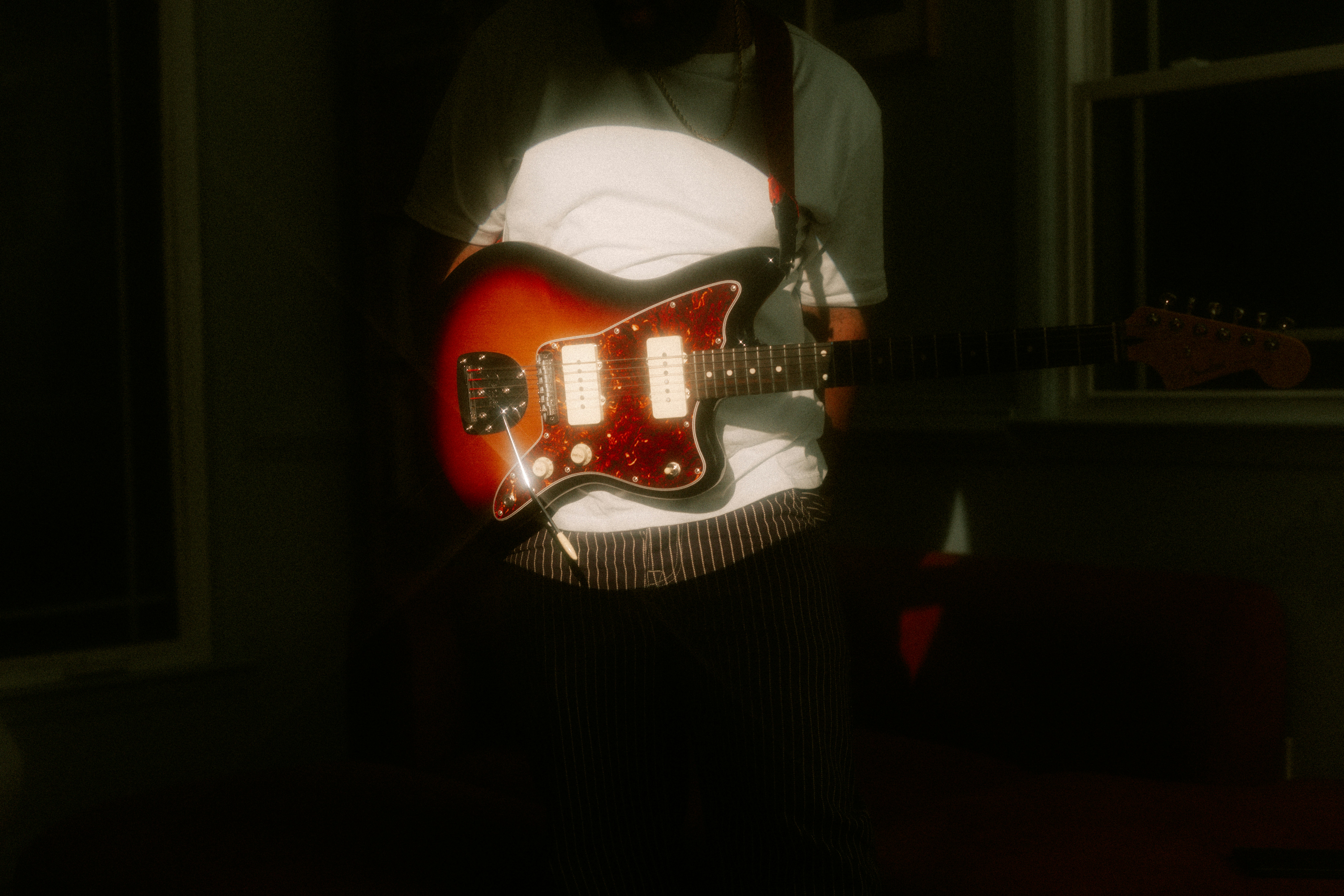 A person in a white t-shirt holding a sunlit sunburst electric guitar.