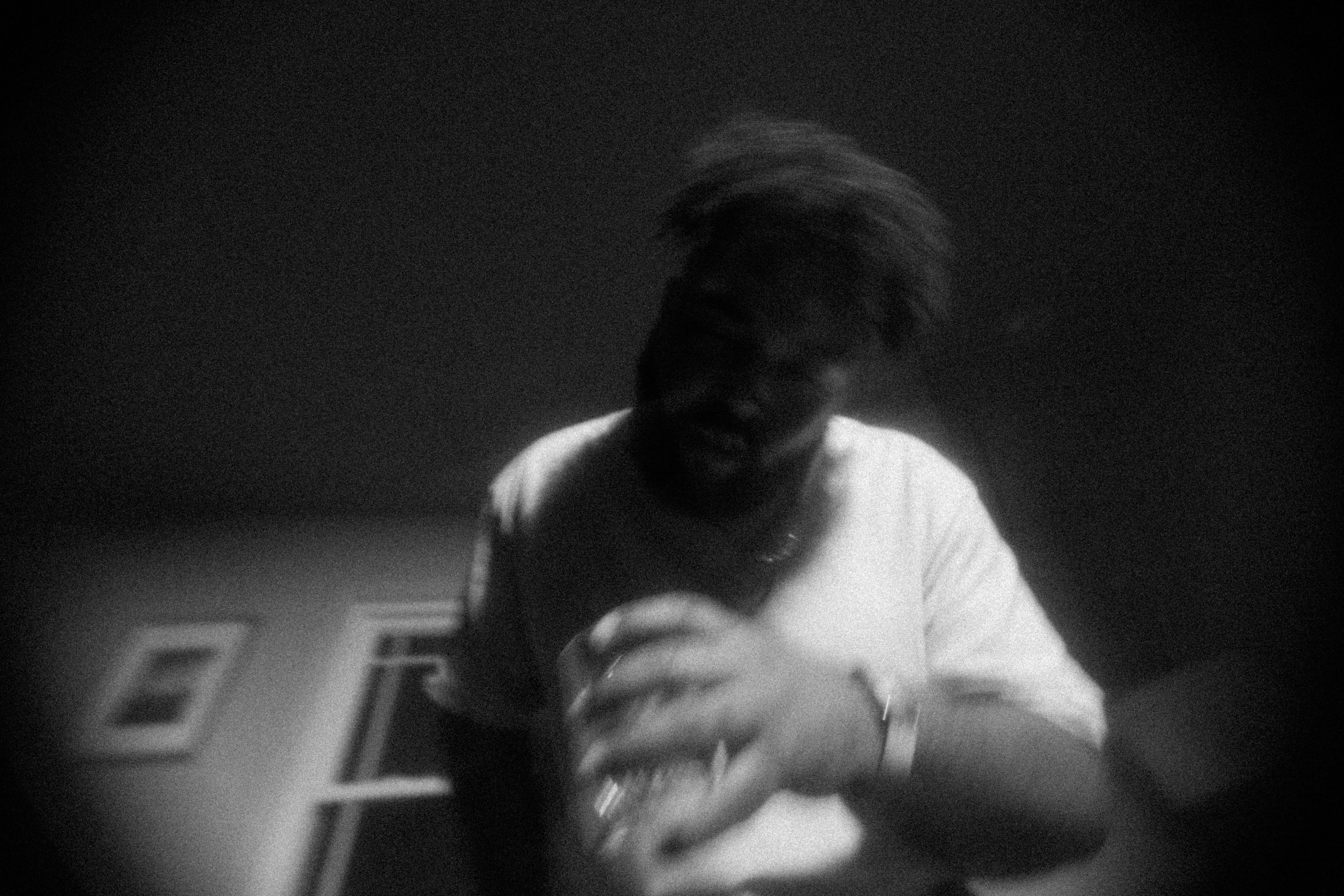 A person in a white t-shirt holding a glass in a dimly lit room.