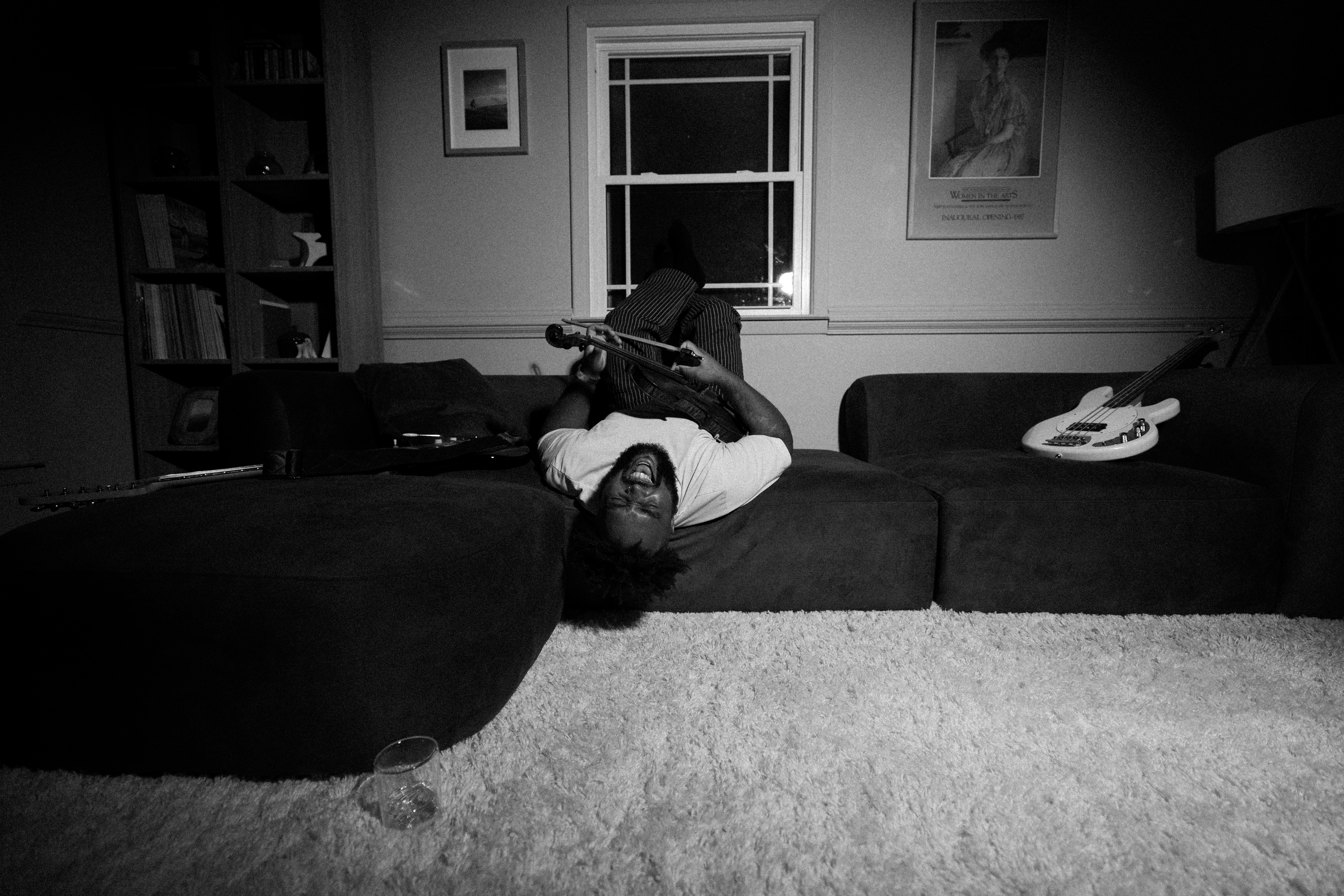 A person laughing while lying upside down on a sofa with a violin.