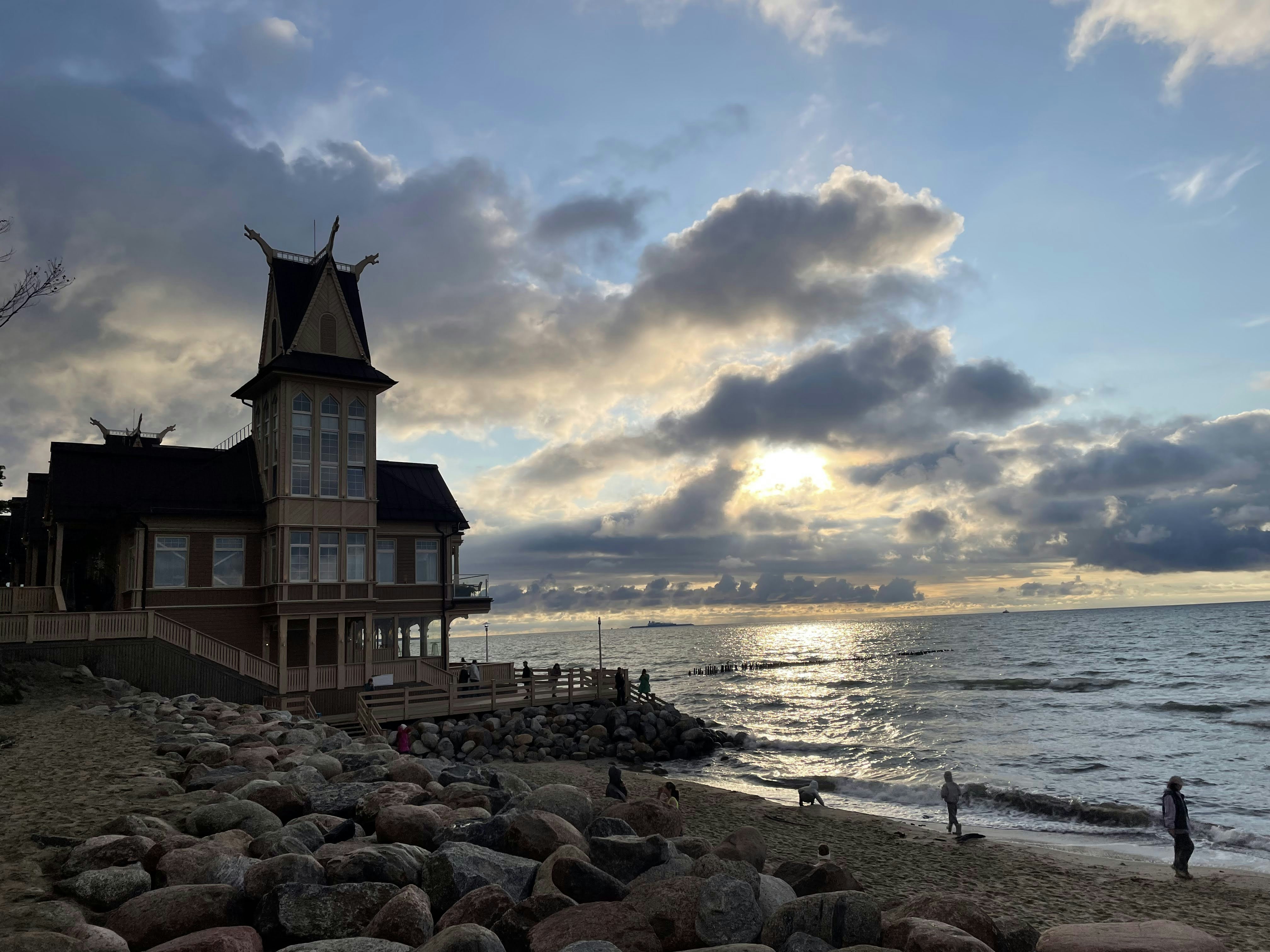 A wooden building with a tall tower on a rocky beach at low sun