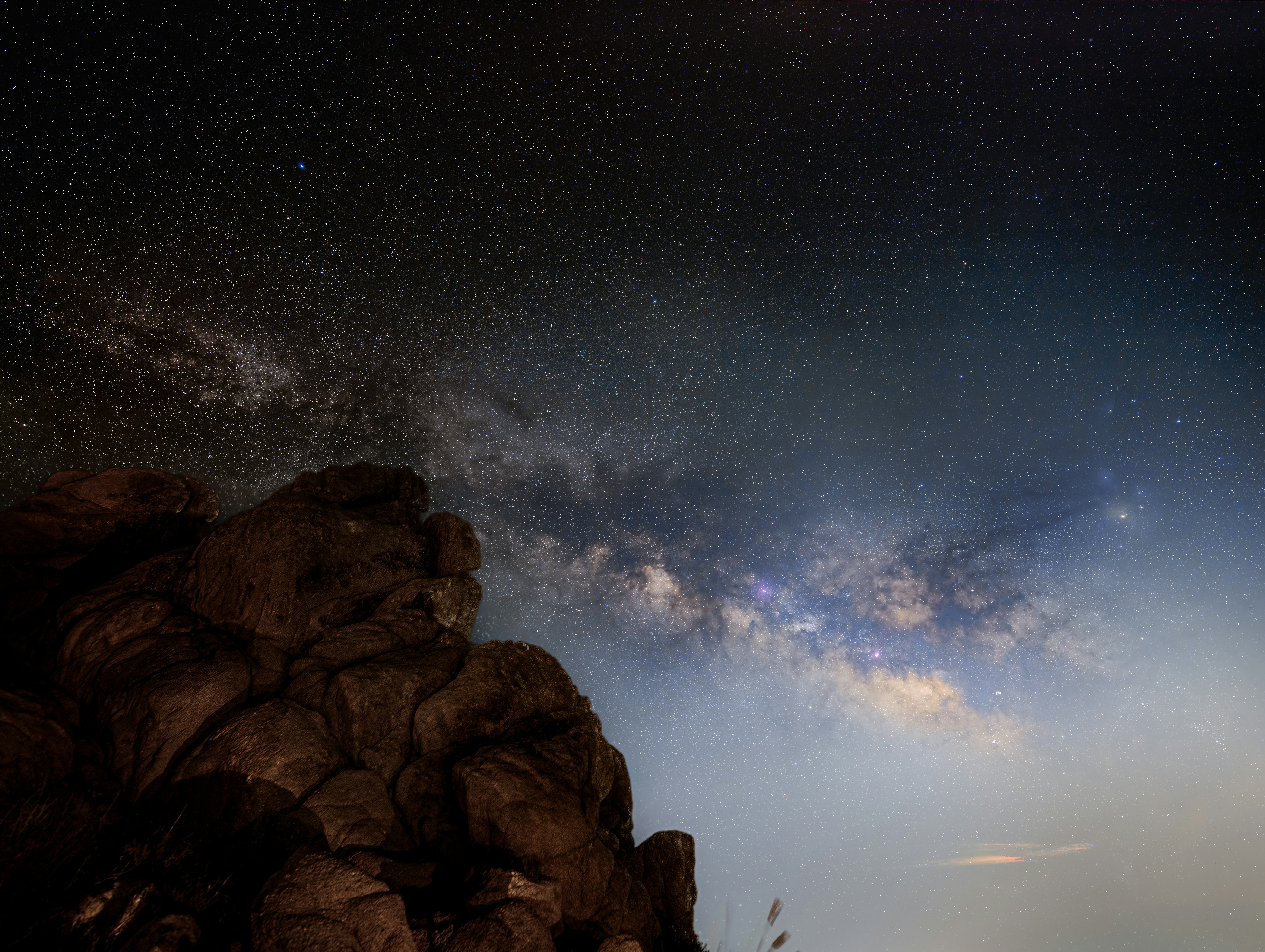 La galaxia de la Vía Láctea brillando sobre un oscuro afloramiento rocoso por la noche
