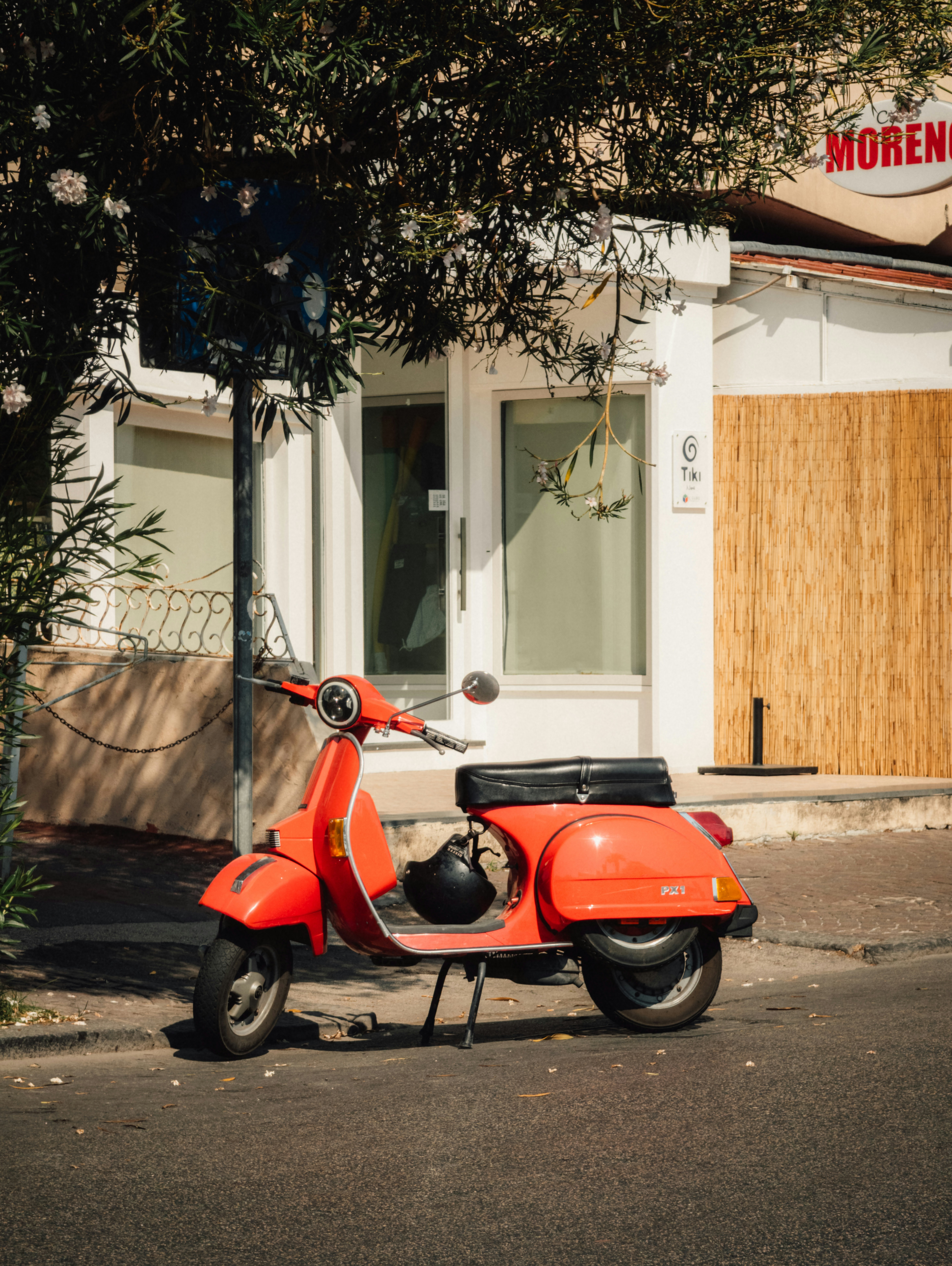 A bright orange scooter parked on a sidewalk beside a white building.