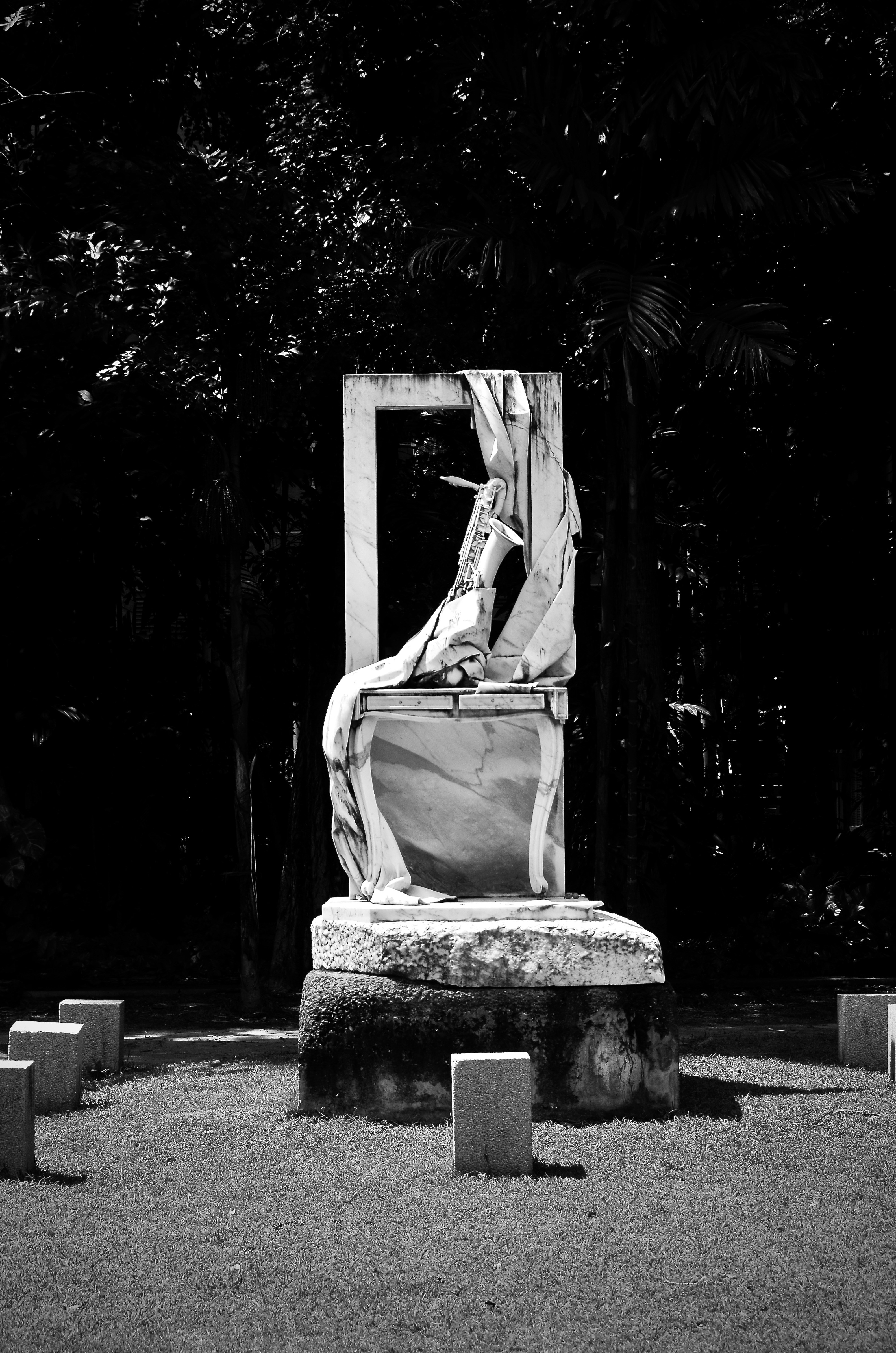Una scultura in marmo di un sassofono e un tessuto drappeggiato su un piedistallo.