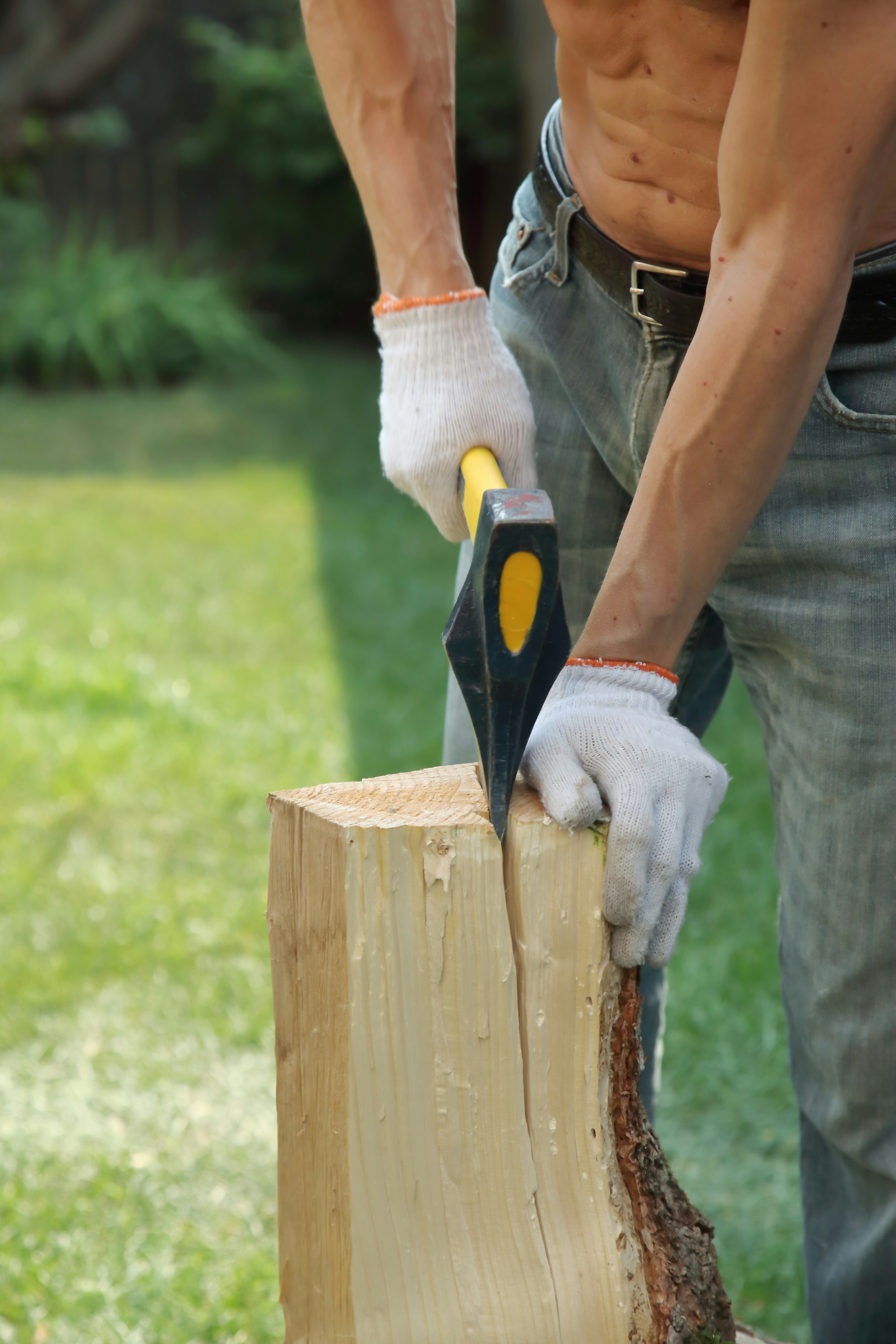 A person in white gloves splitting a wooden log with an axe outdoors.