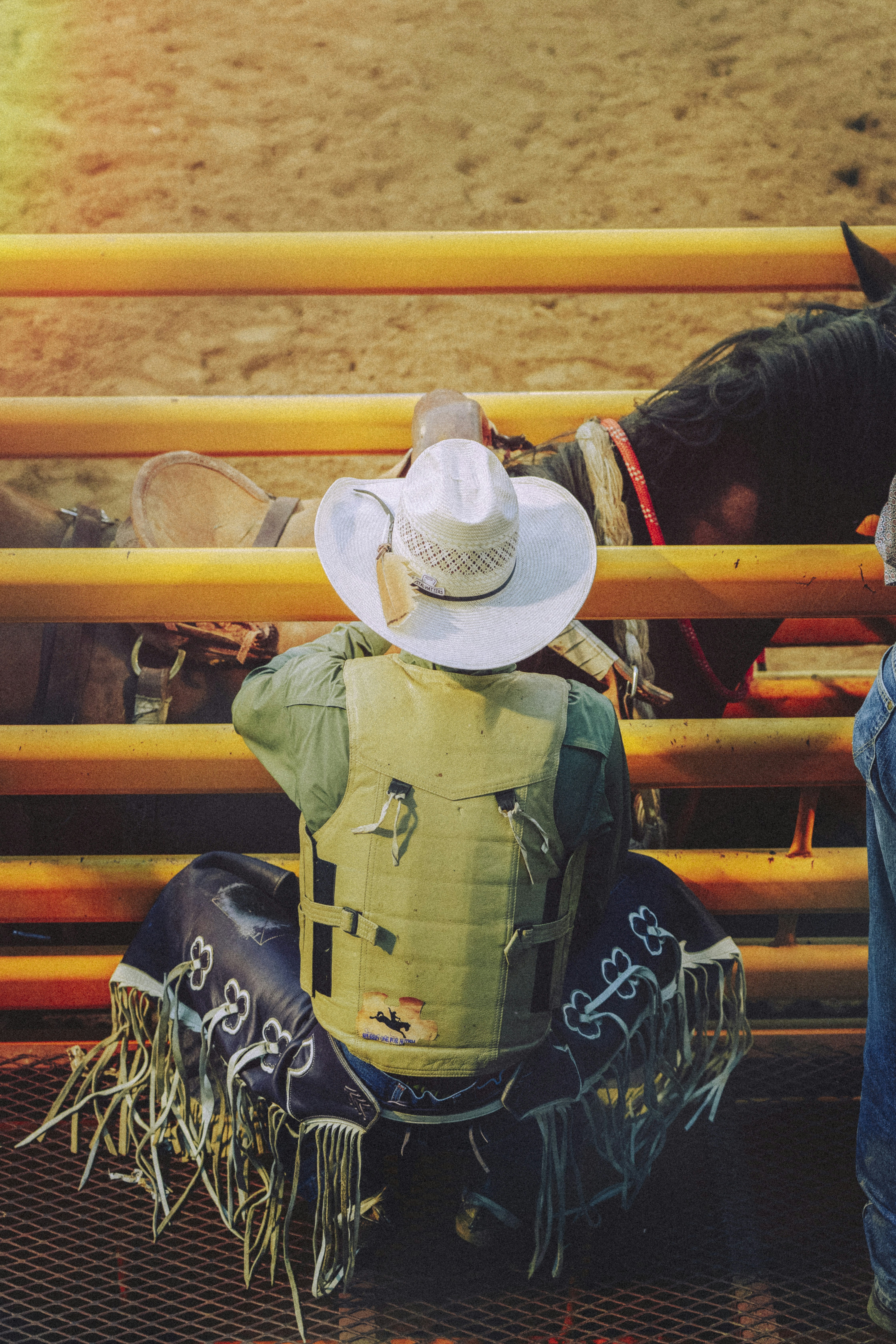 A bull rider in a white cowboy hat and protective vest by yellow chutes.
