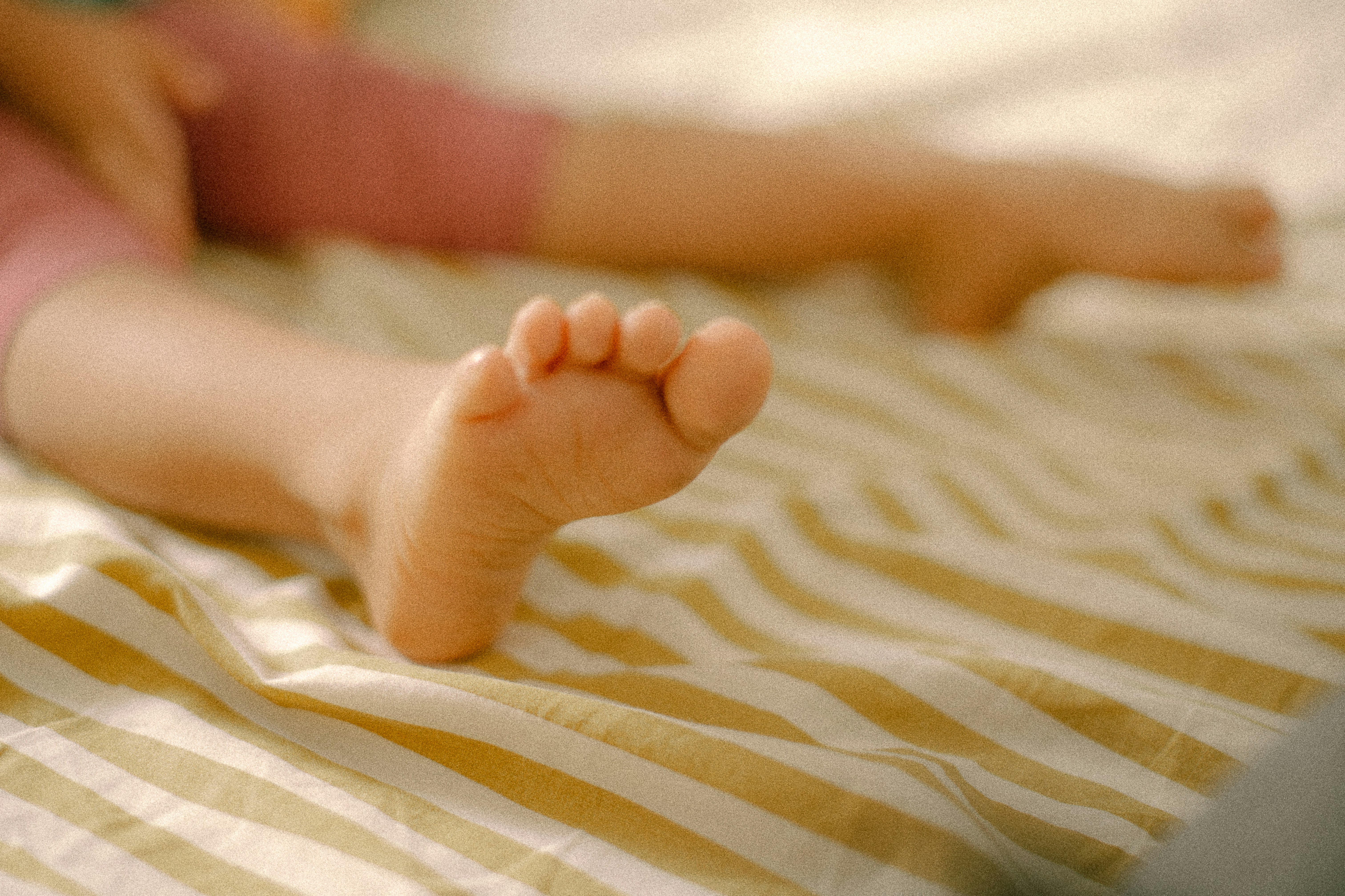 A child's bare foot resting on a yellow and white striped bed sheet.