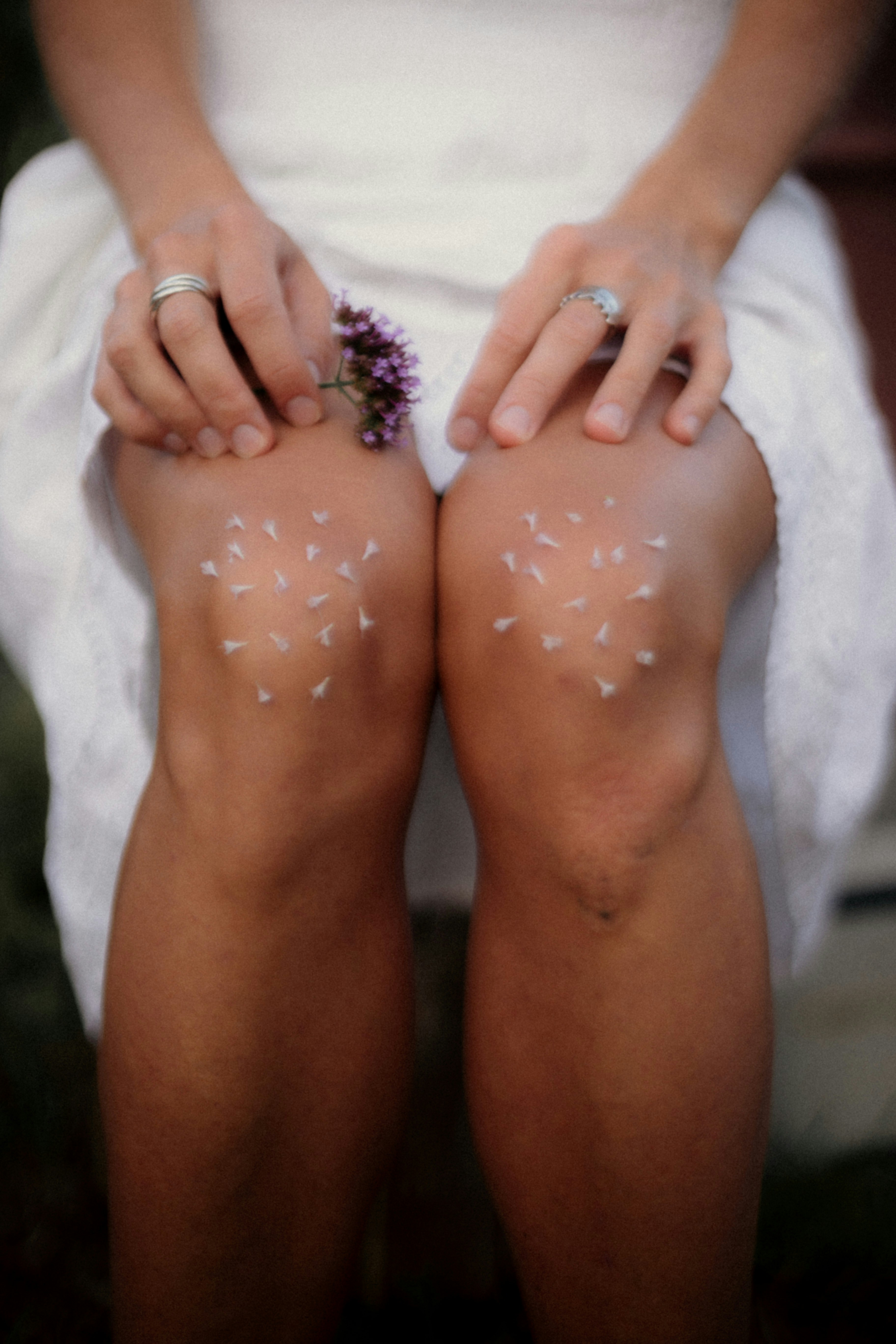 A person in a white dress with small flower petals on their knees.