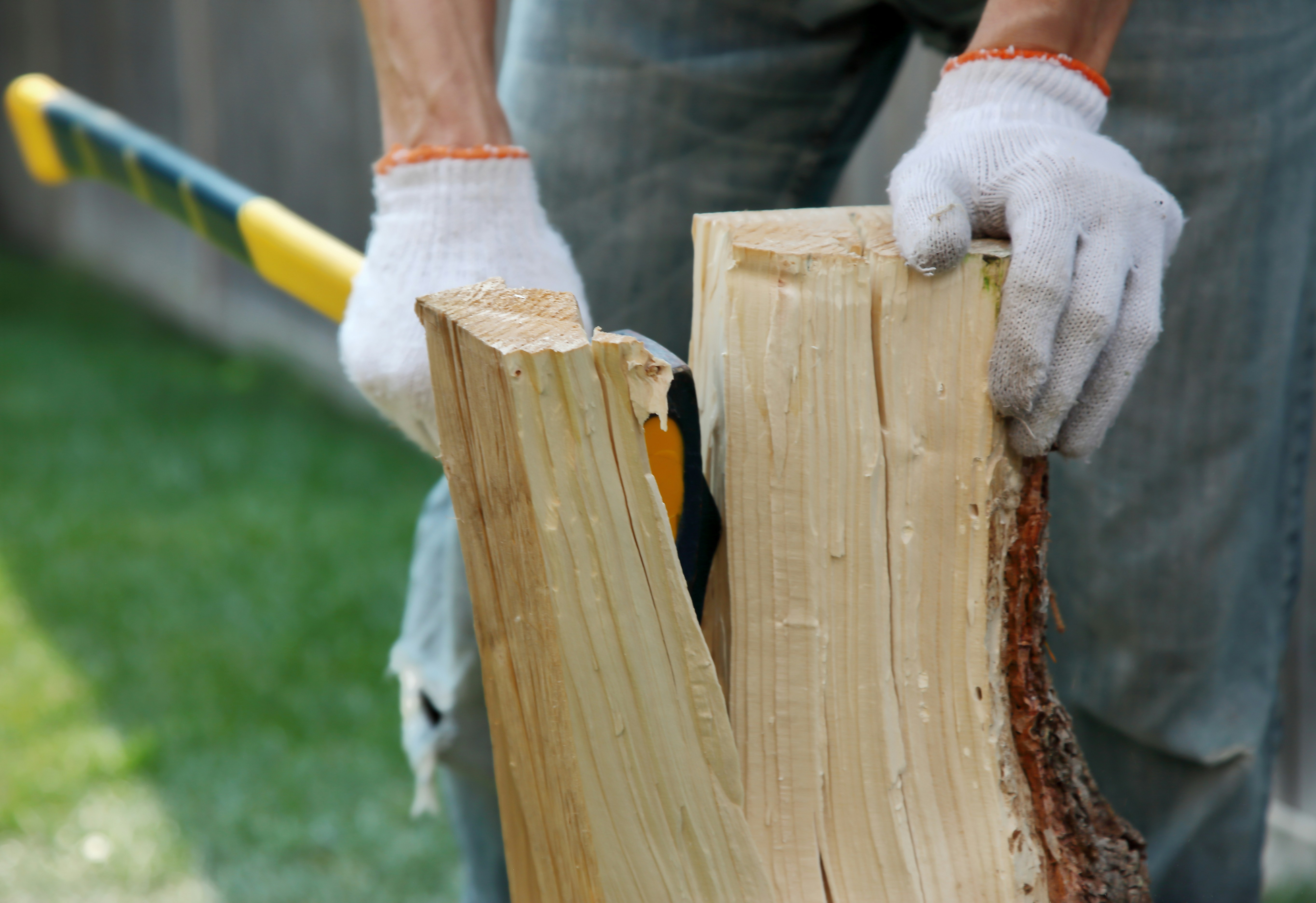 A person in white gloves splitting a wooden log with an axe.