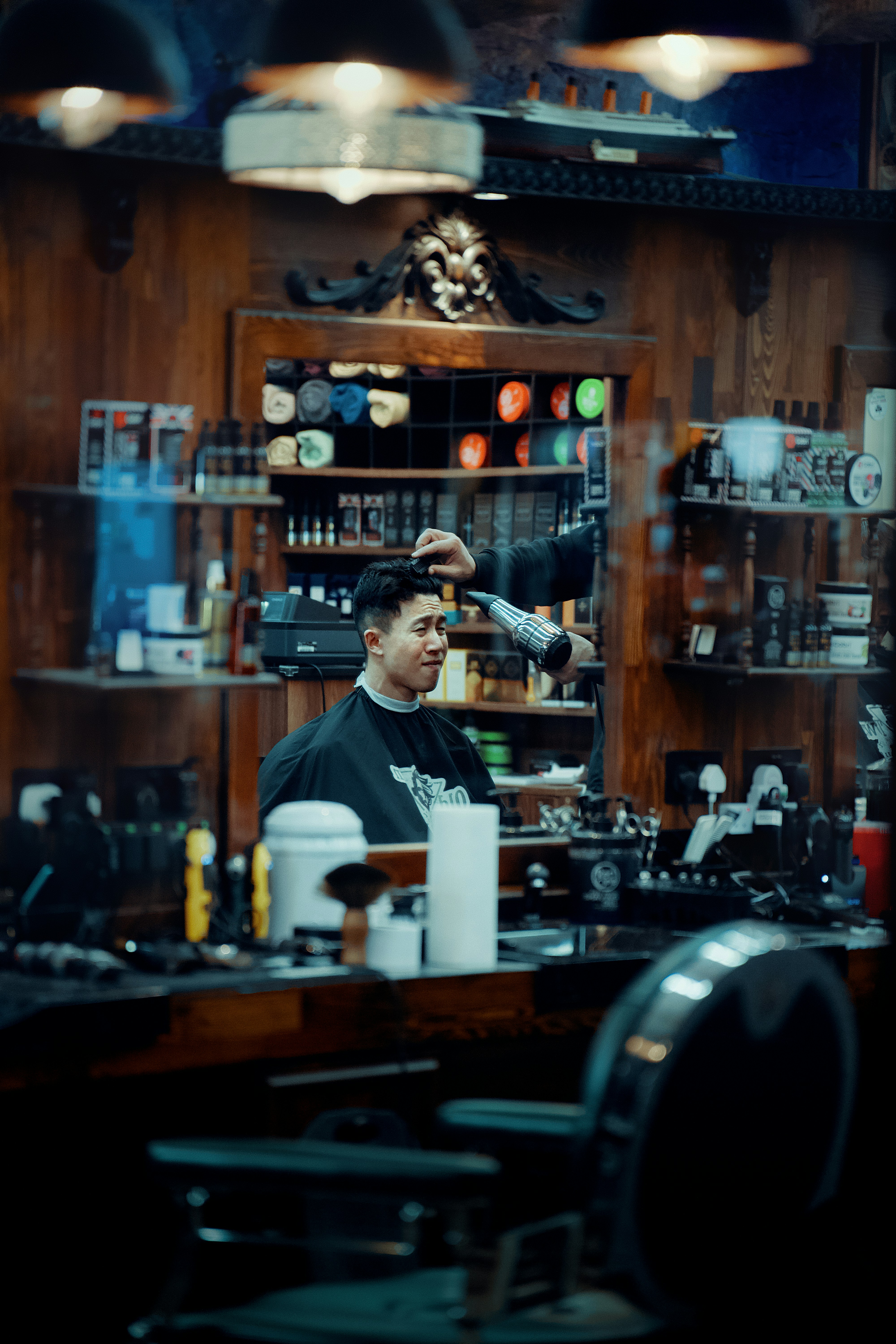 A barber using a hair dryer on a man in a wooden barbershop