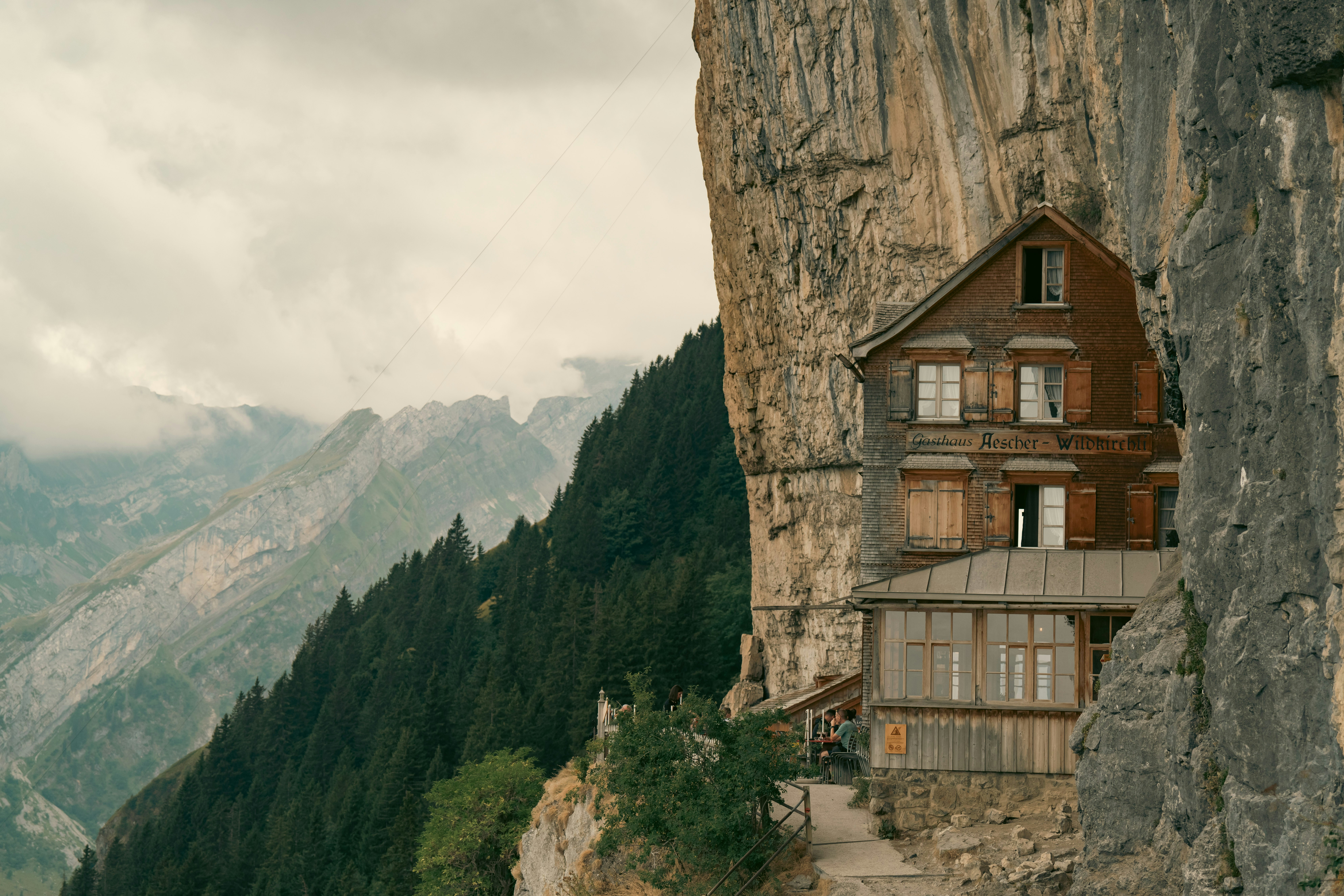 The Aescher guesthouse built into a cliffside overlooking a forested mountain valley