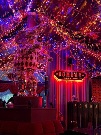 A mirrored elephant statue under strings of red and blue lights at a rooftop bar