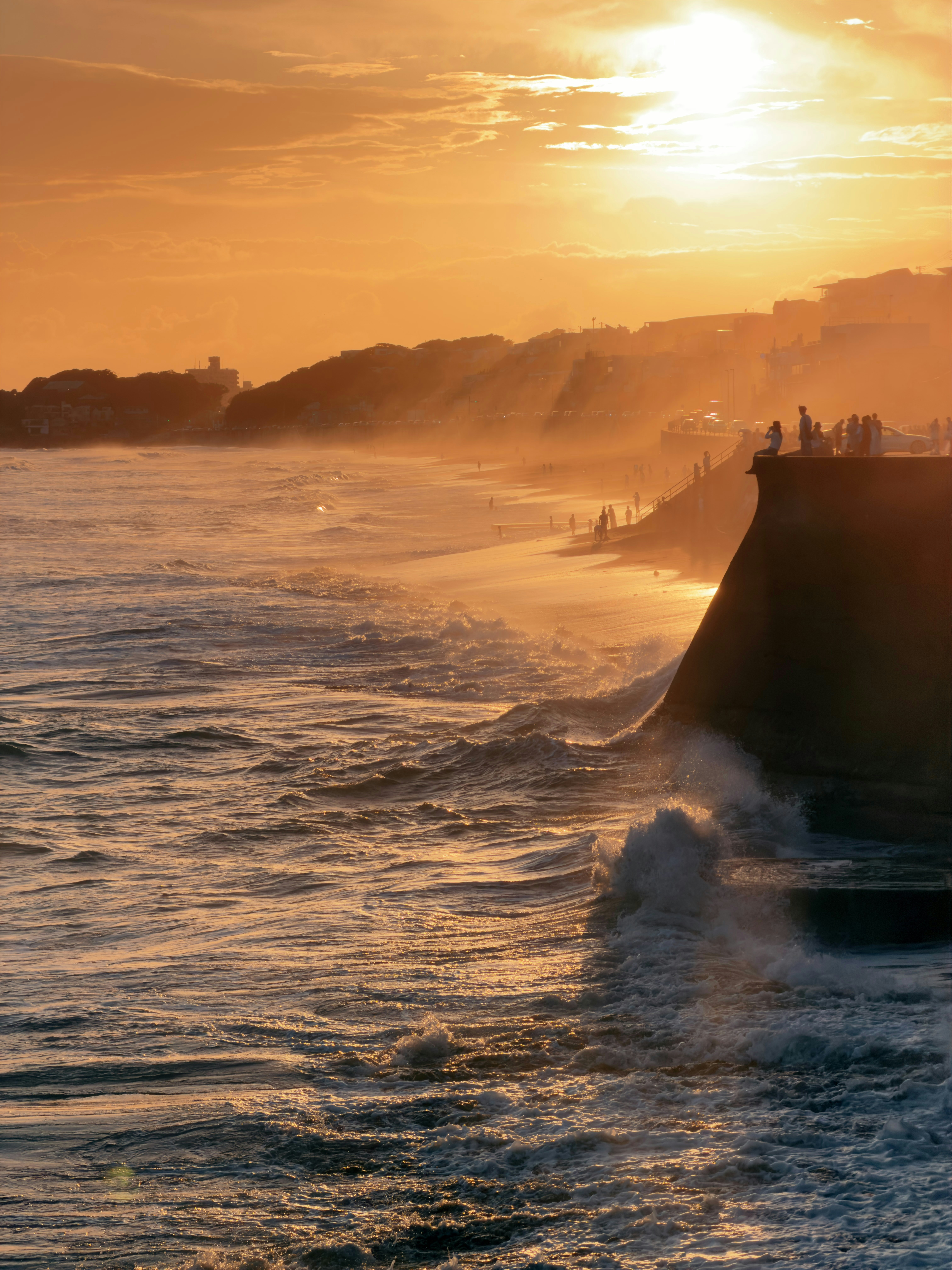 Waves crashing against a concrete wall under a warm orange sky at low sun.