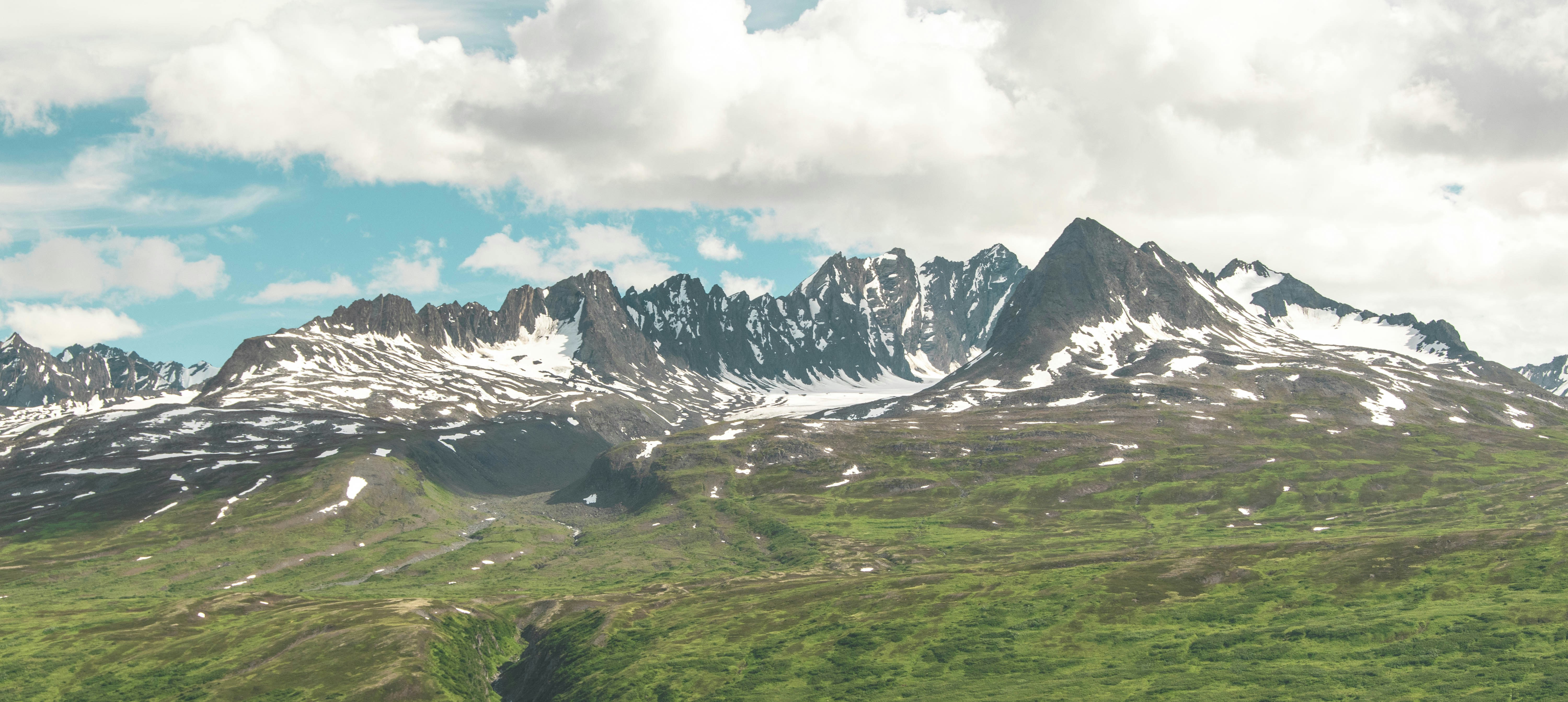 Snow-capped mountain peaks rising above a green valley under a cloudy sky