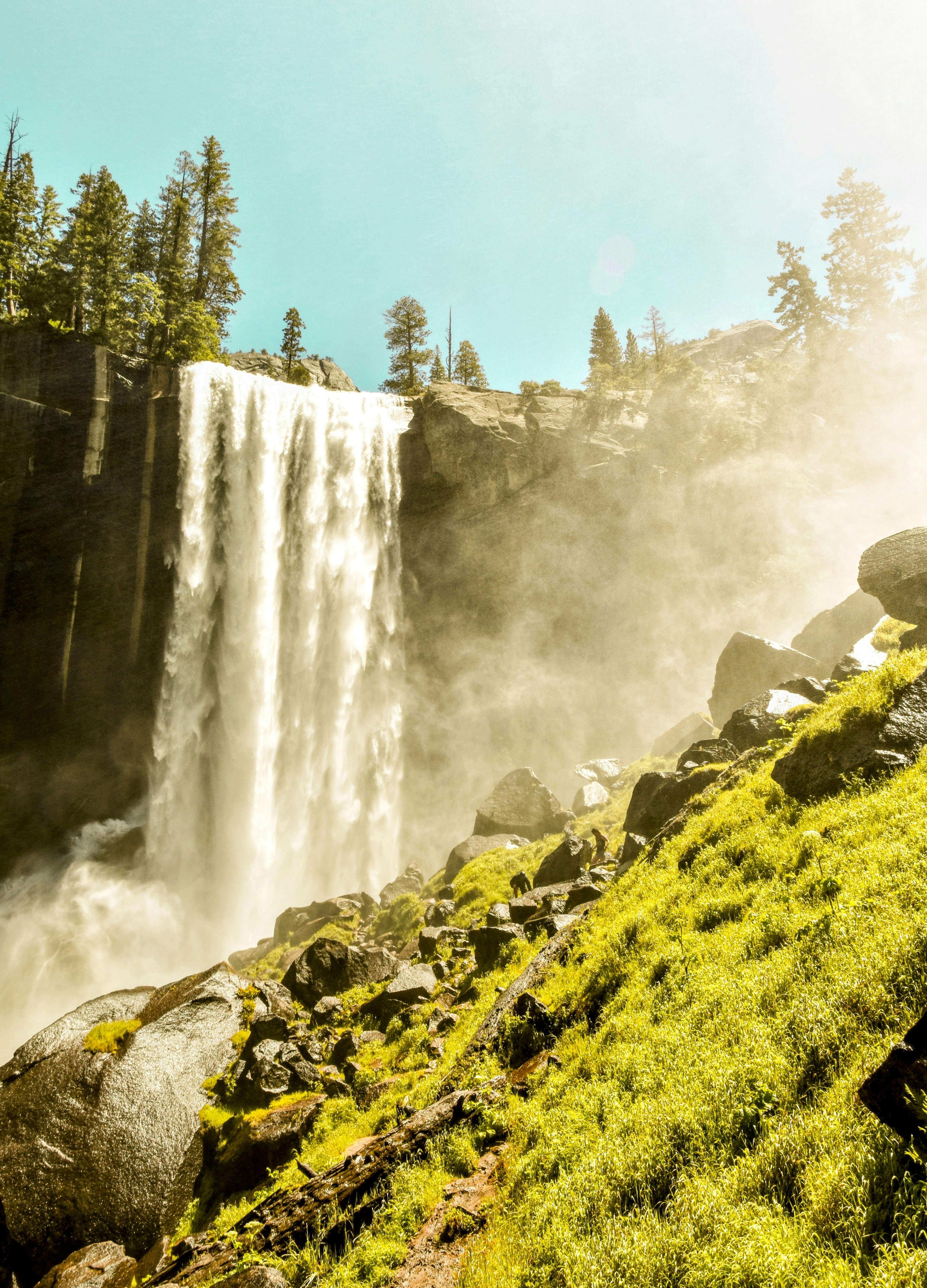 A waterfall cascading over a rocky cliff beside a bright green grassy slope