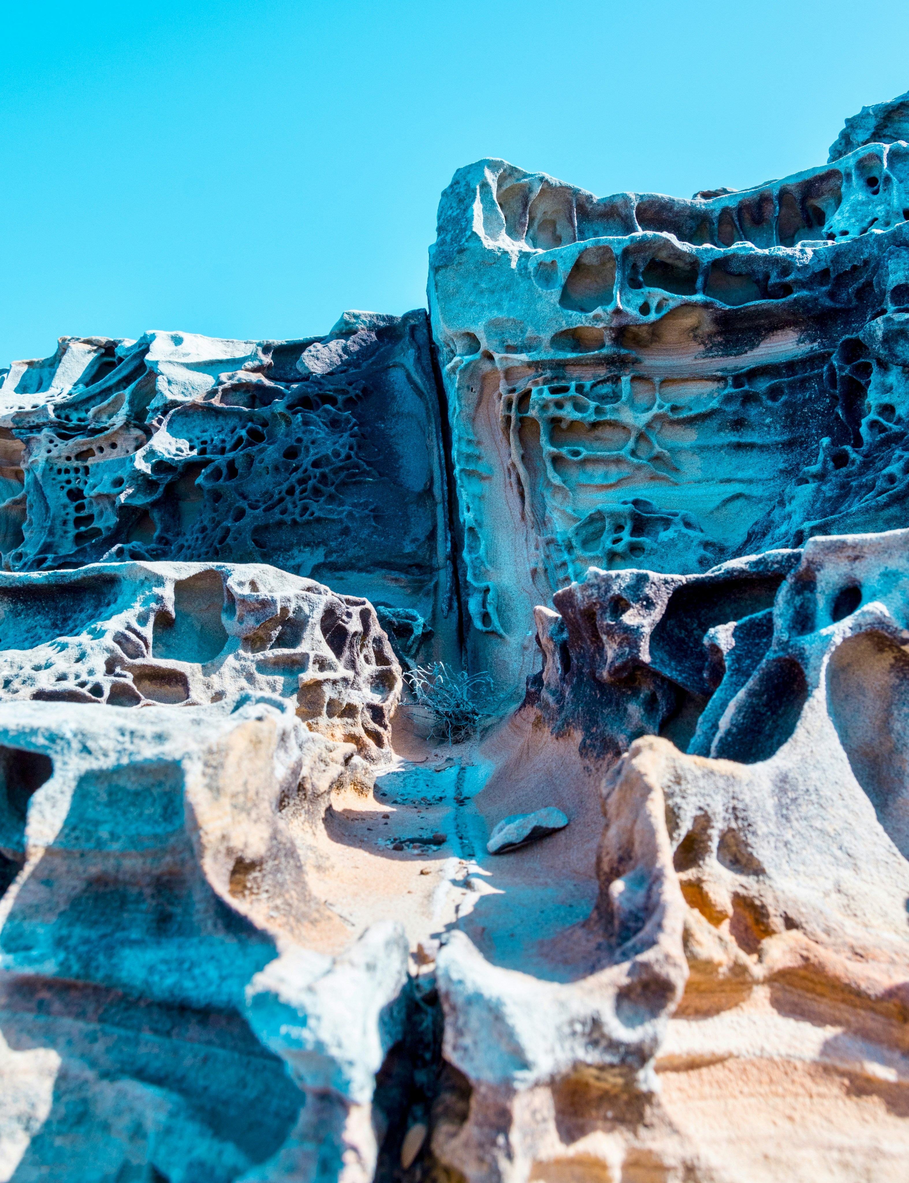 Eroded sandstone rock formations with honeycomb textures under a clear blue sky.