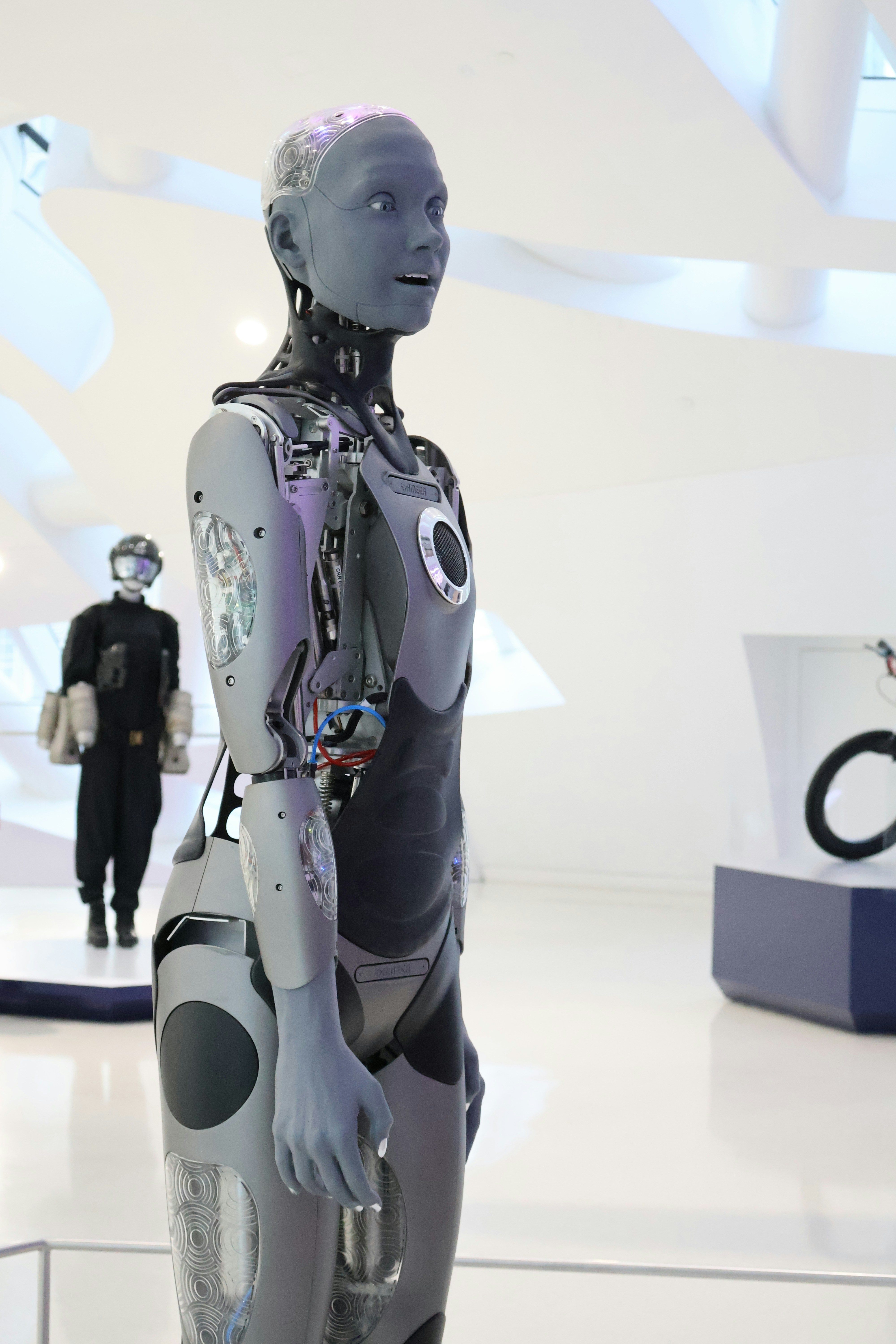 Un robot humanoïde gris aux articulations mécaniques exposées dans une galerie blanche éclatante
