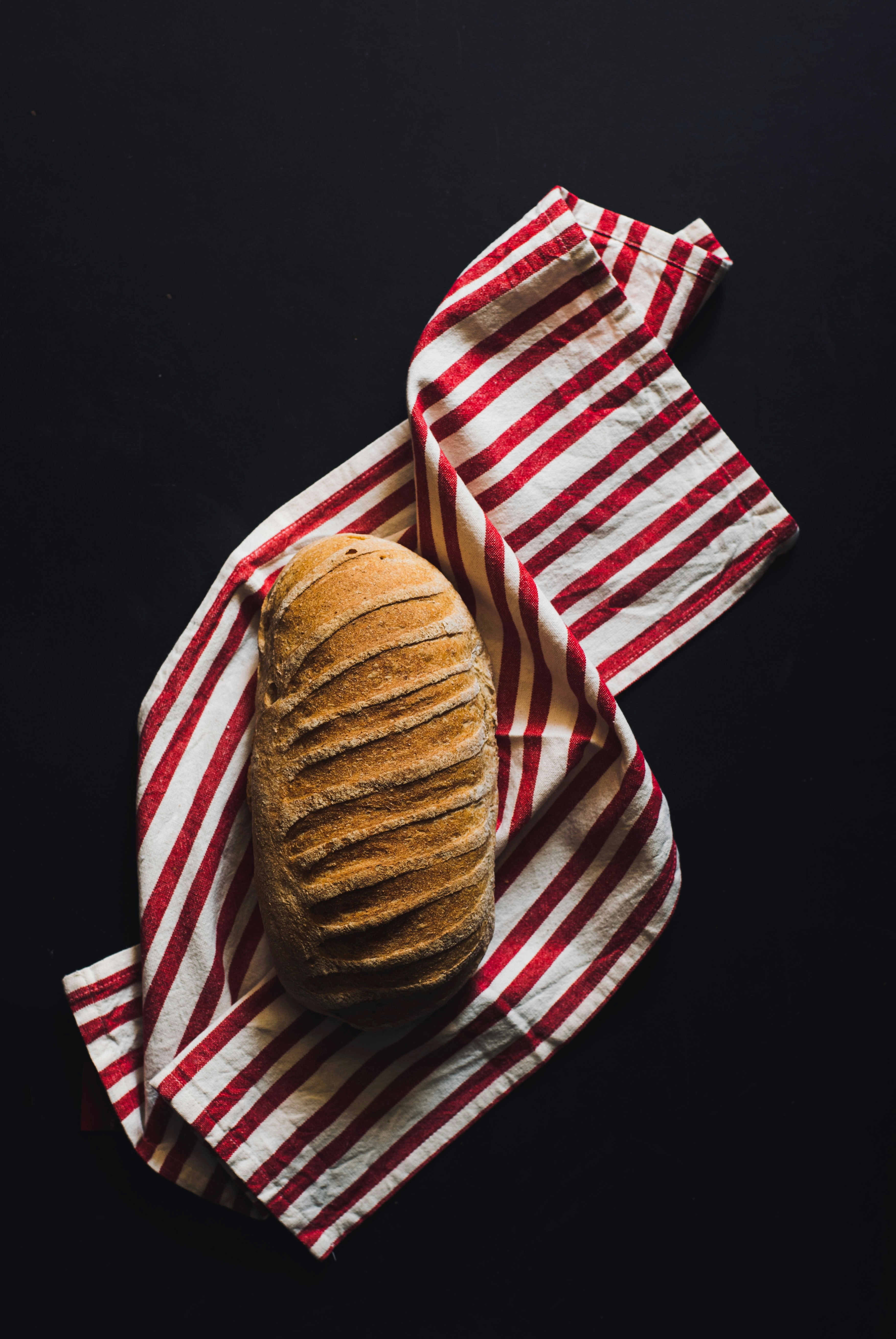 Ein Laib mit eingerissenem Sauerteigbrot auf einem rot-weiß gestreiften Tuch.