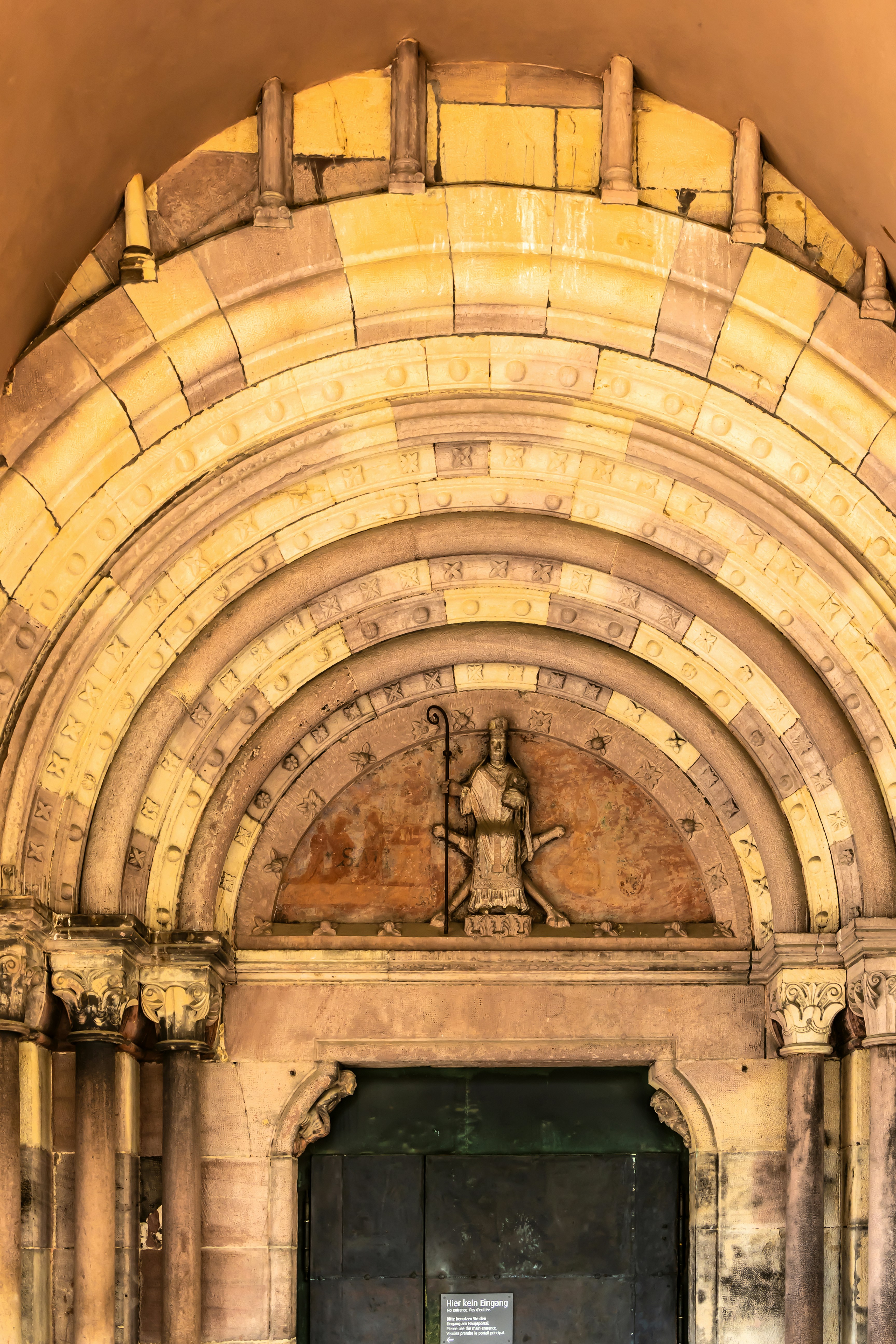 Une arche de pierre avec une figure sculptée tenant un bâton au-dessus d’une porte