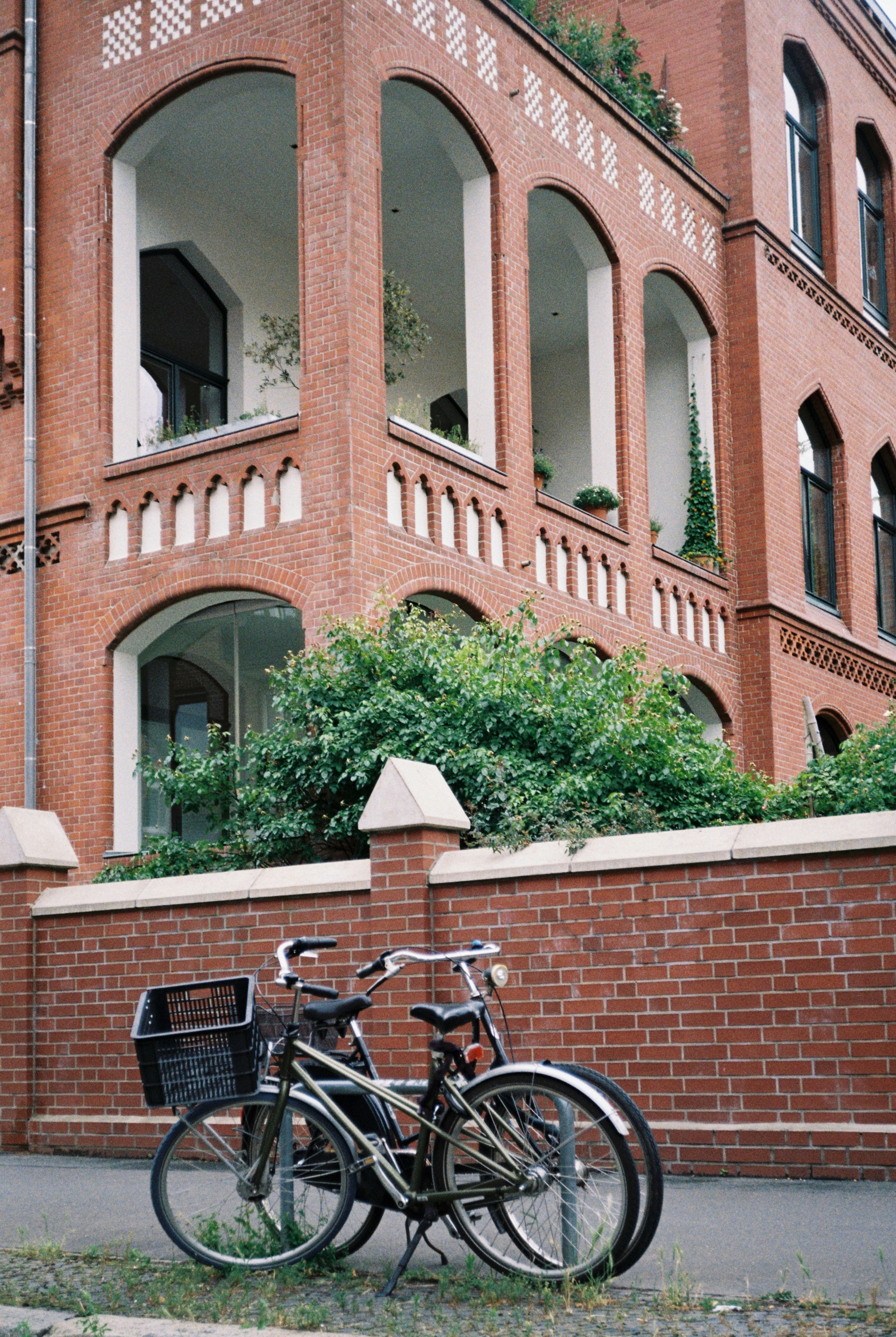 Two bicycles parked against a red brick wall in front of a building.