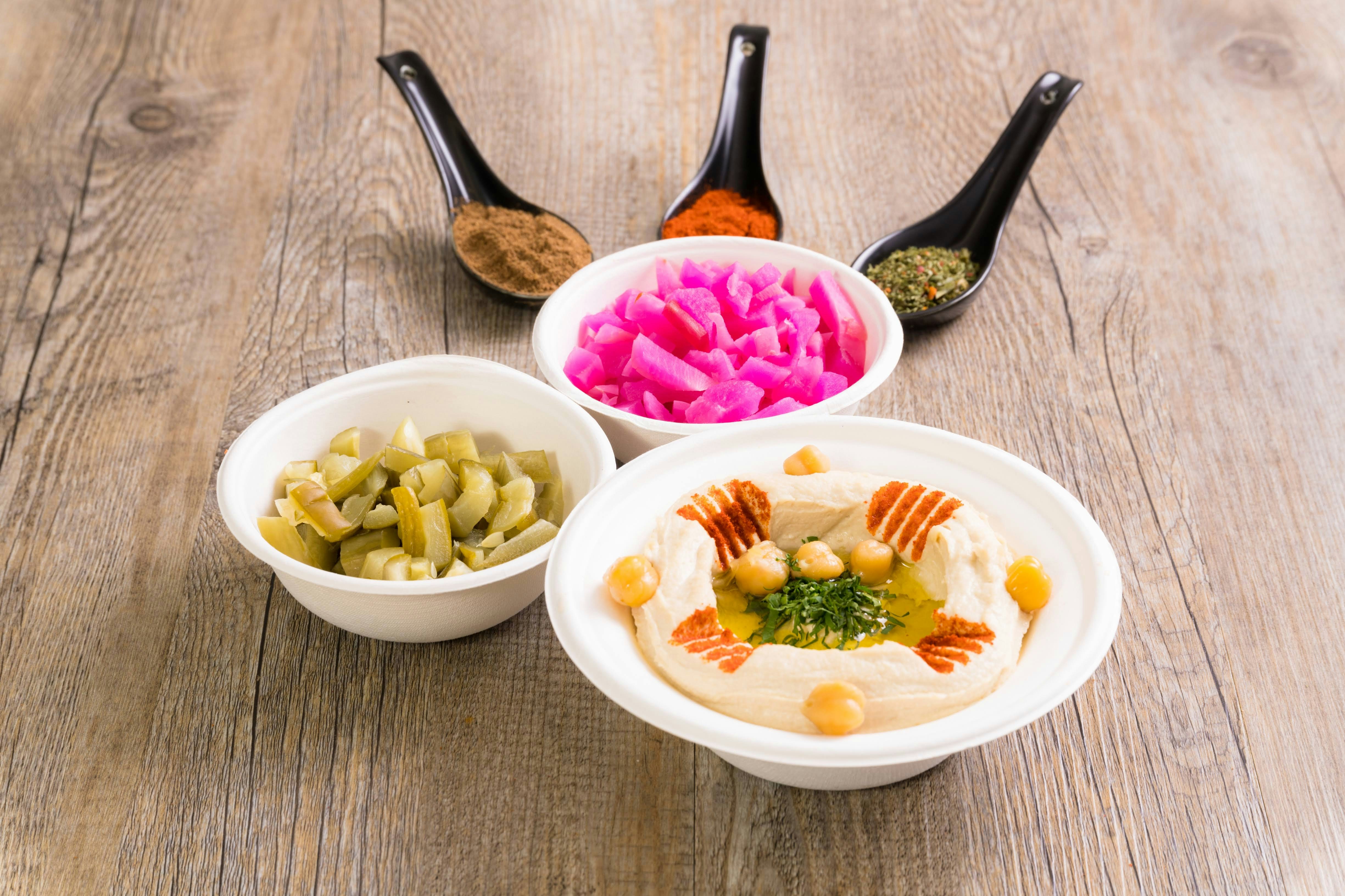 Hummus with chickpeas, pickled turnips, and chopped pickles on a wooden table
