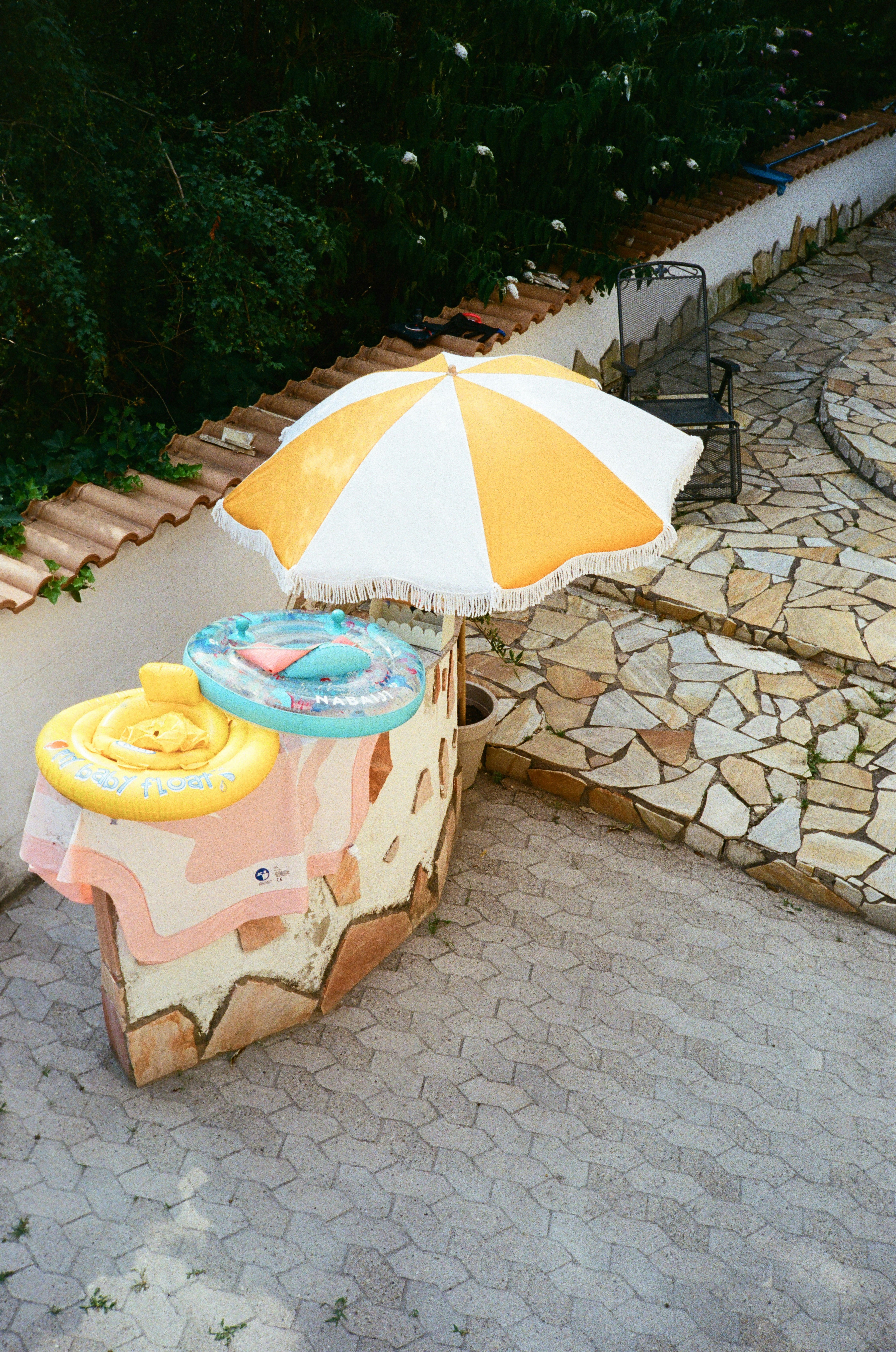 A yellow and white striped umbrella over pool floats on a stone wall.