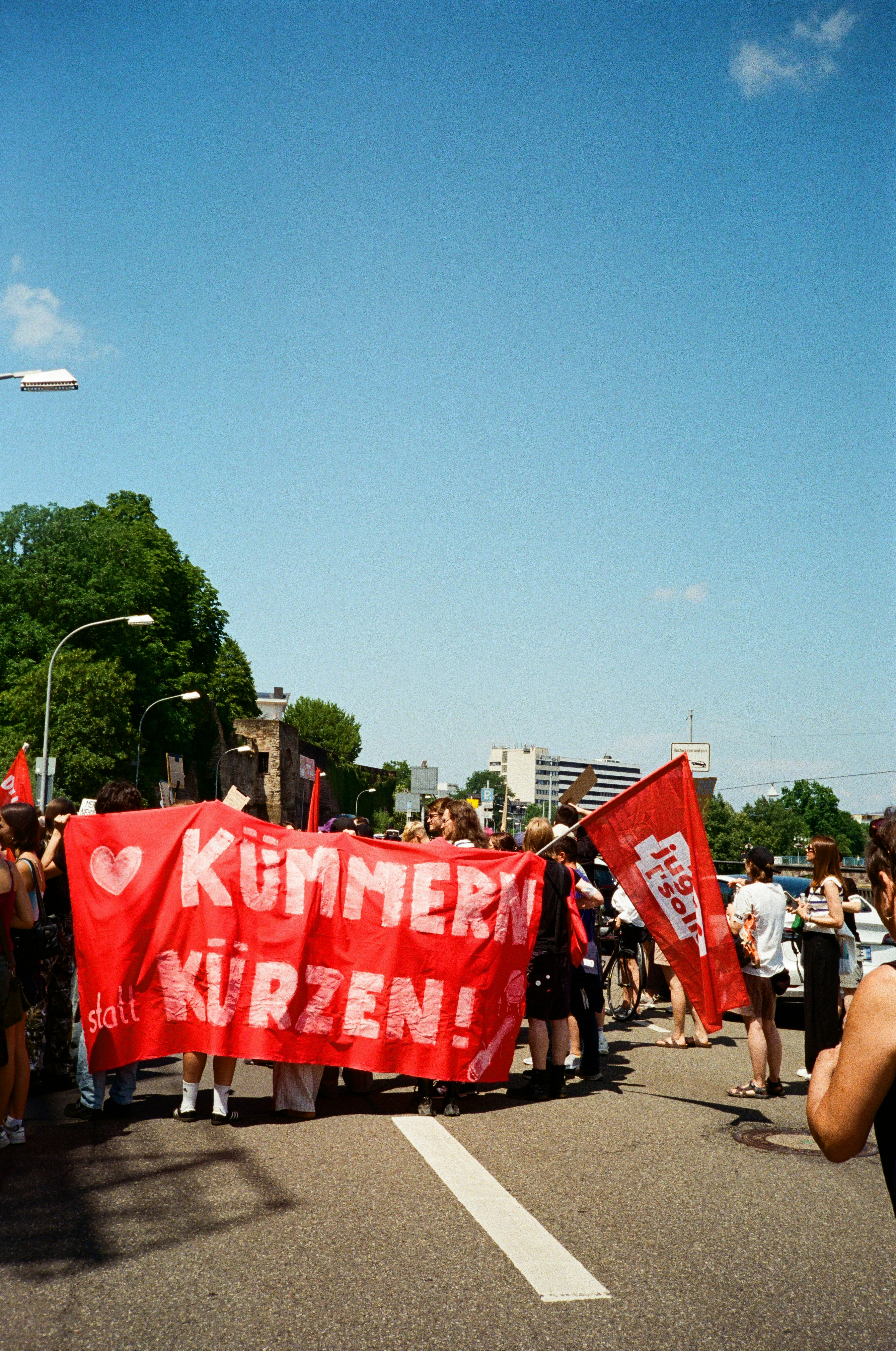A group of people holding a red banner reading "Kümmern statt Kürzen!" on a street.