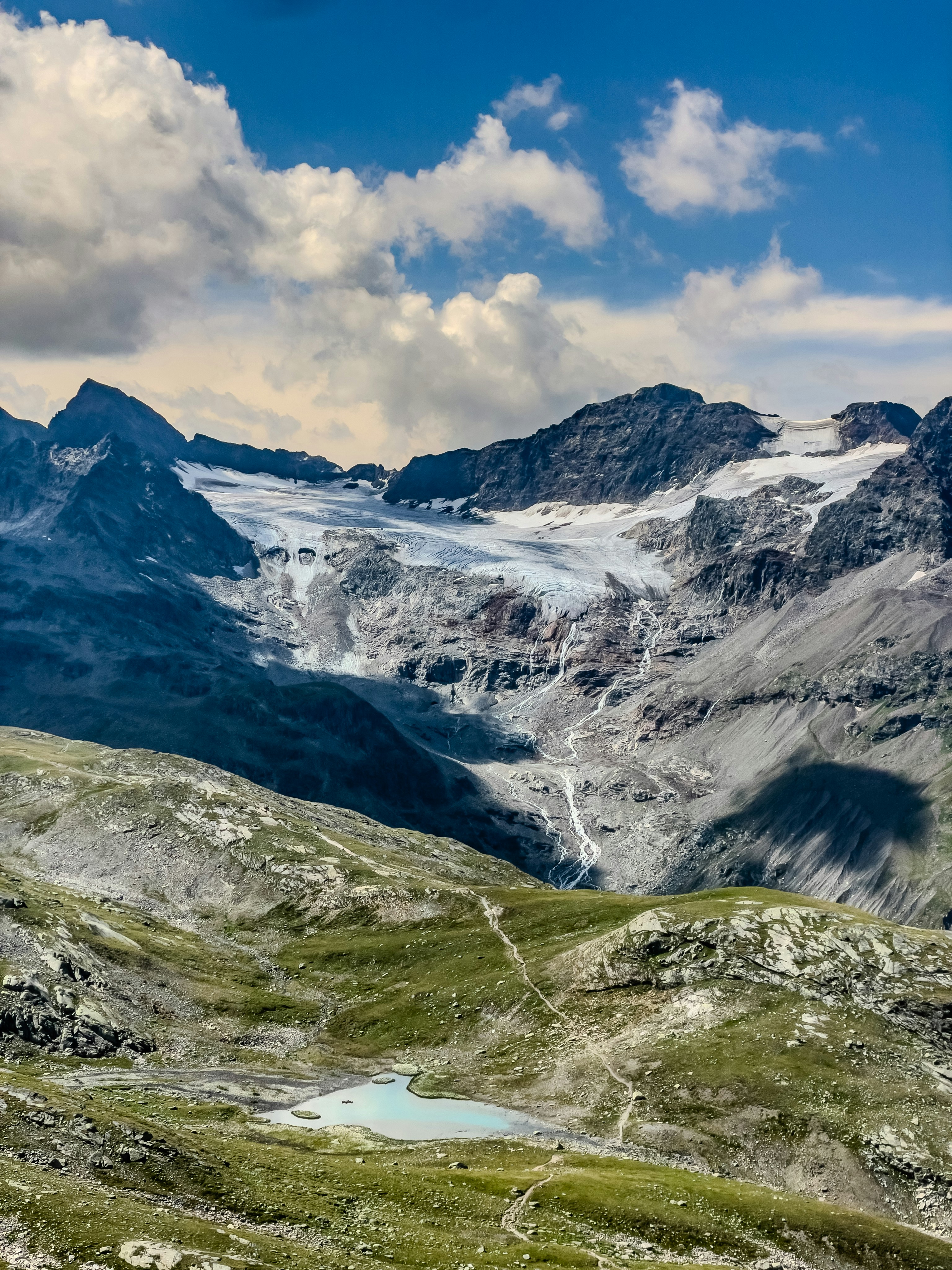 A glacier flowing down a rocky mountain slope toward a small turquoise lake.