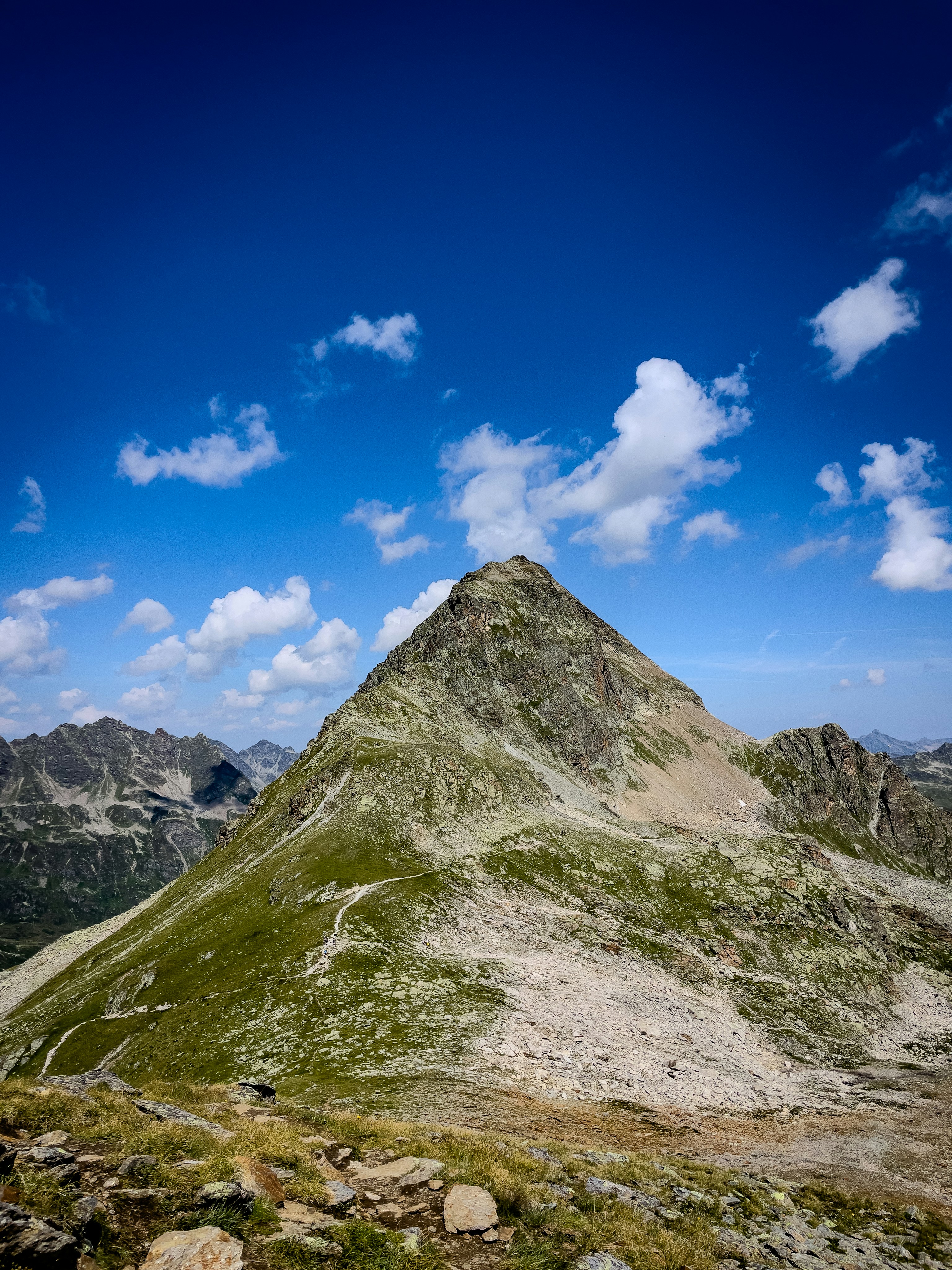 A rocky mountain peak with a winding trail under a bright blue sky.