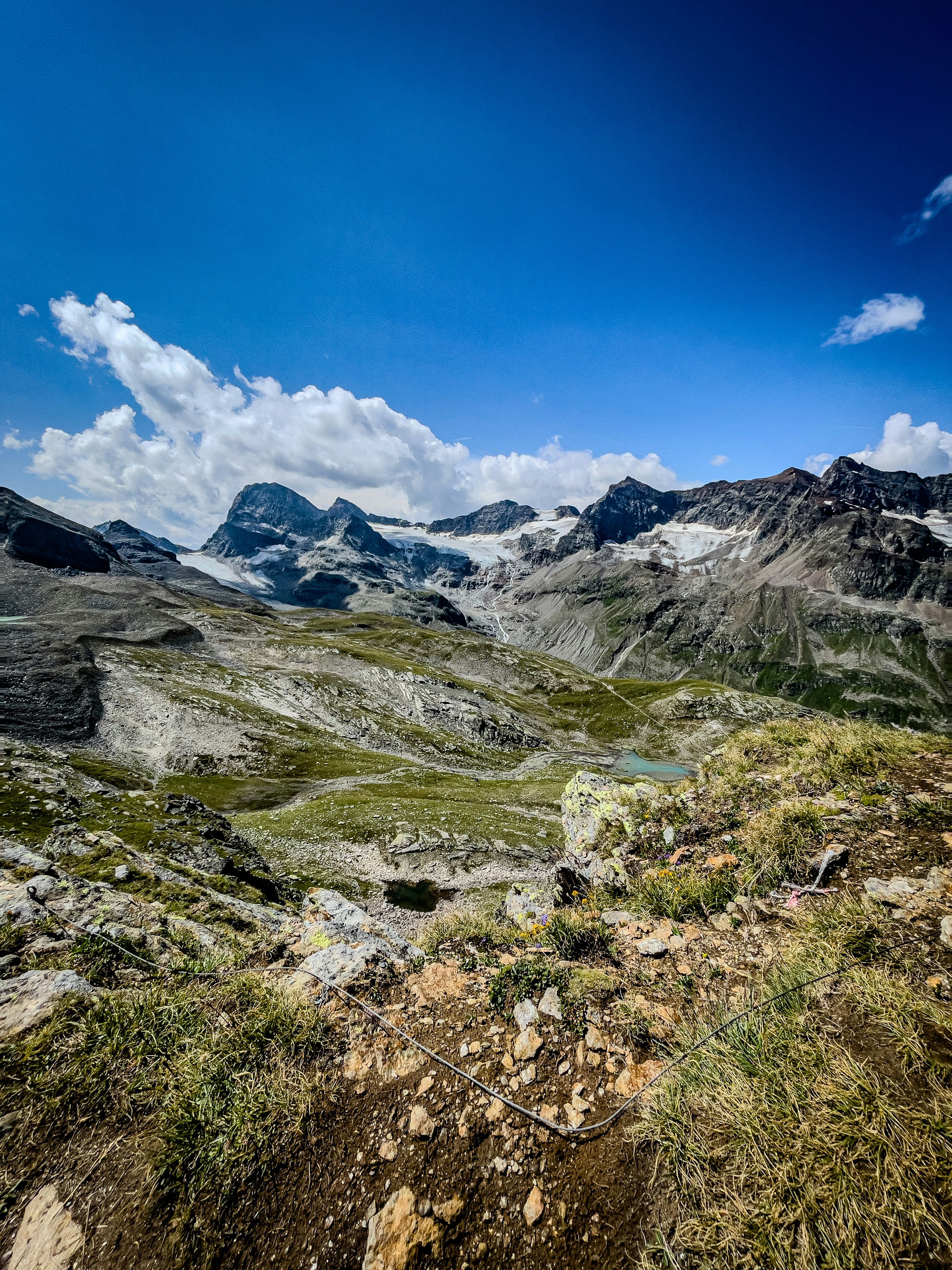 A rocky mountain landscape with a glacier under a bright blue sky.
