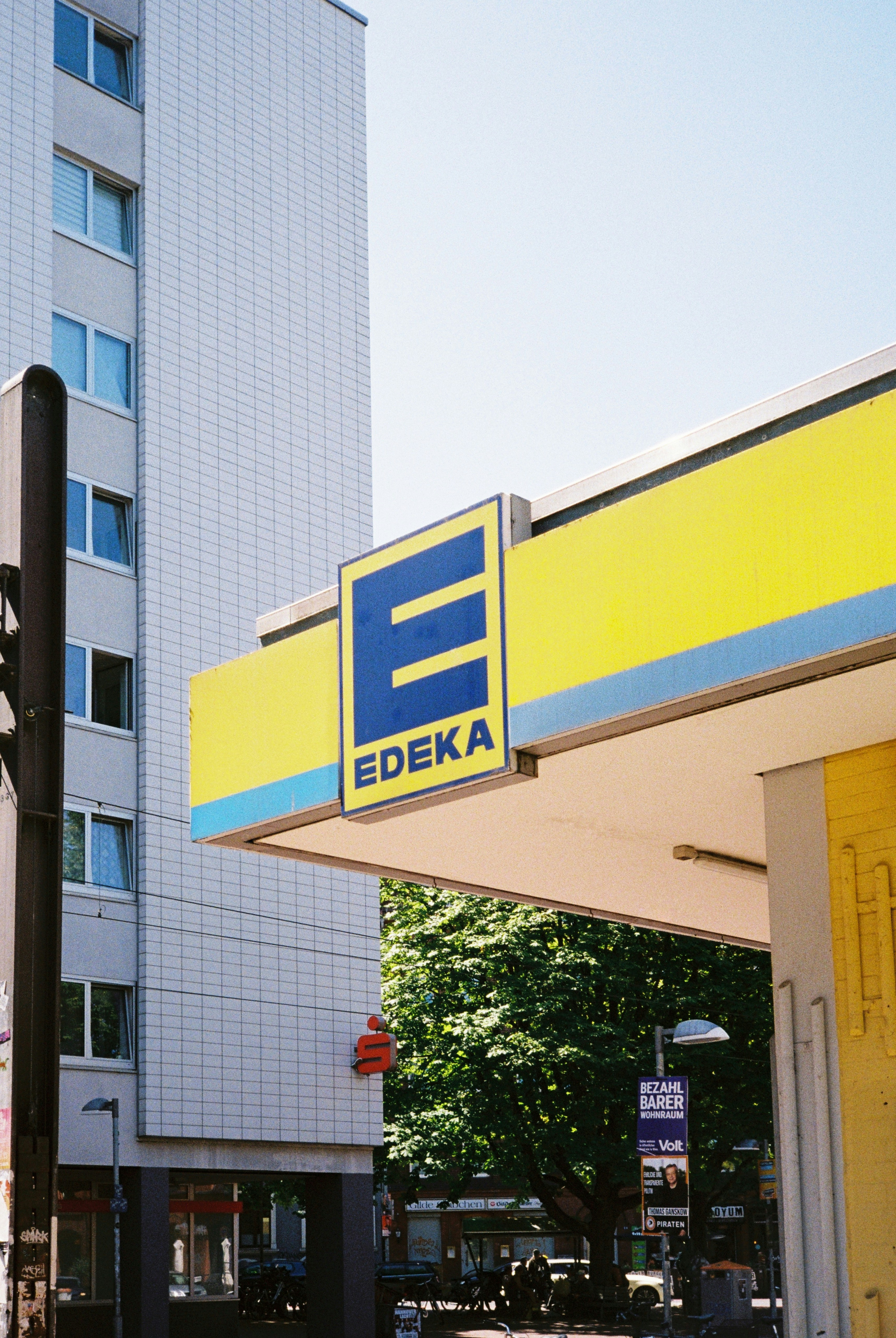 An Edeka supermarket sign on a yellow canopy beside a tall apartment building.