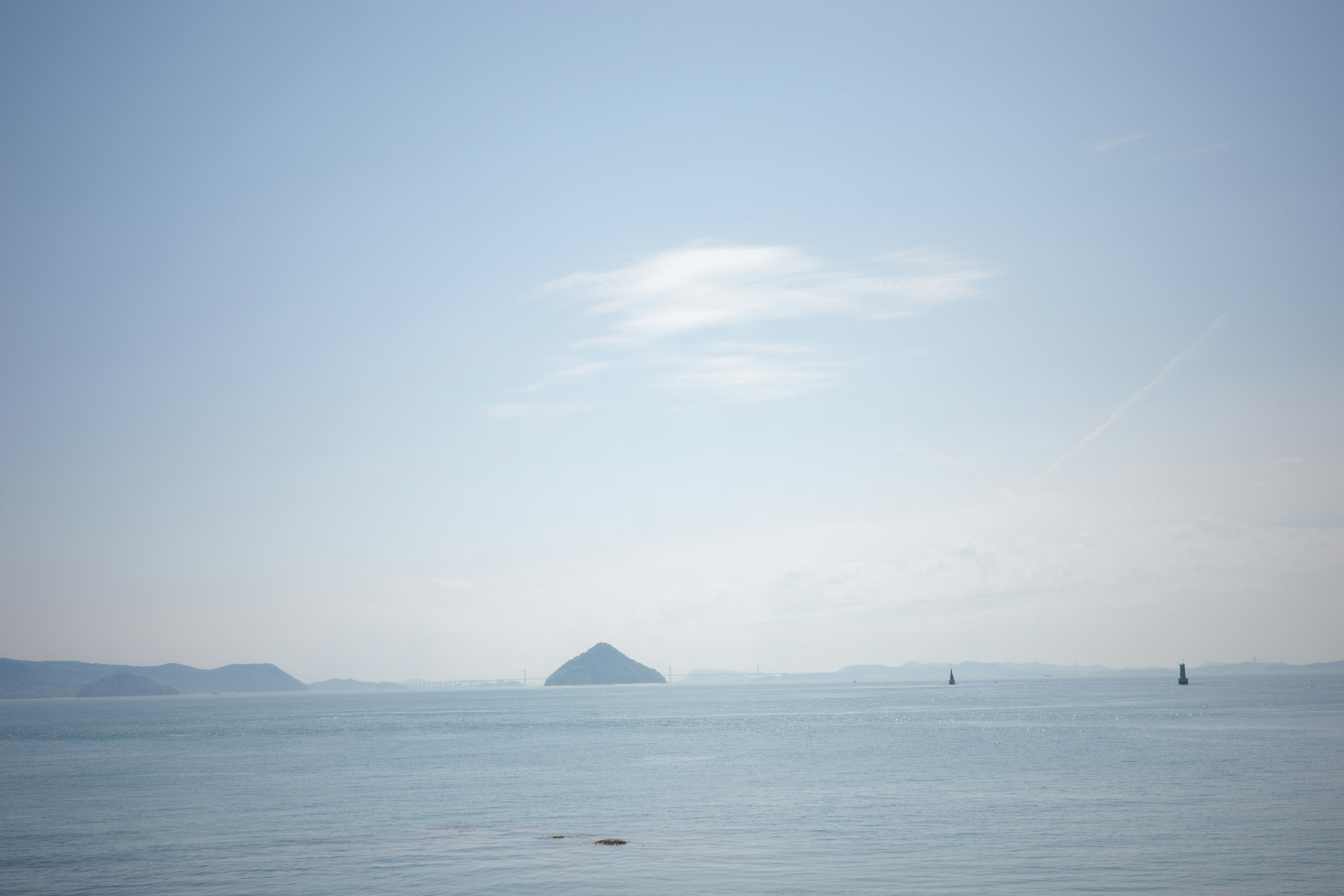 Calm, hazy Inland Sea with a distant conical island and layered islands