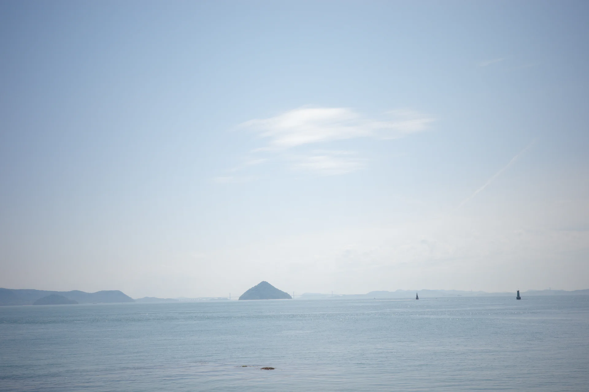 Calm, hazy Inland Sea with a distant conical island and layered islands