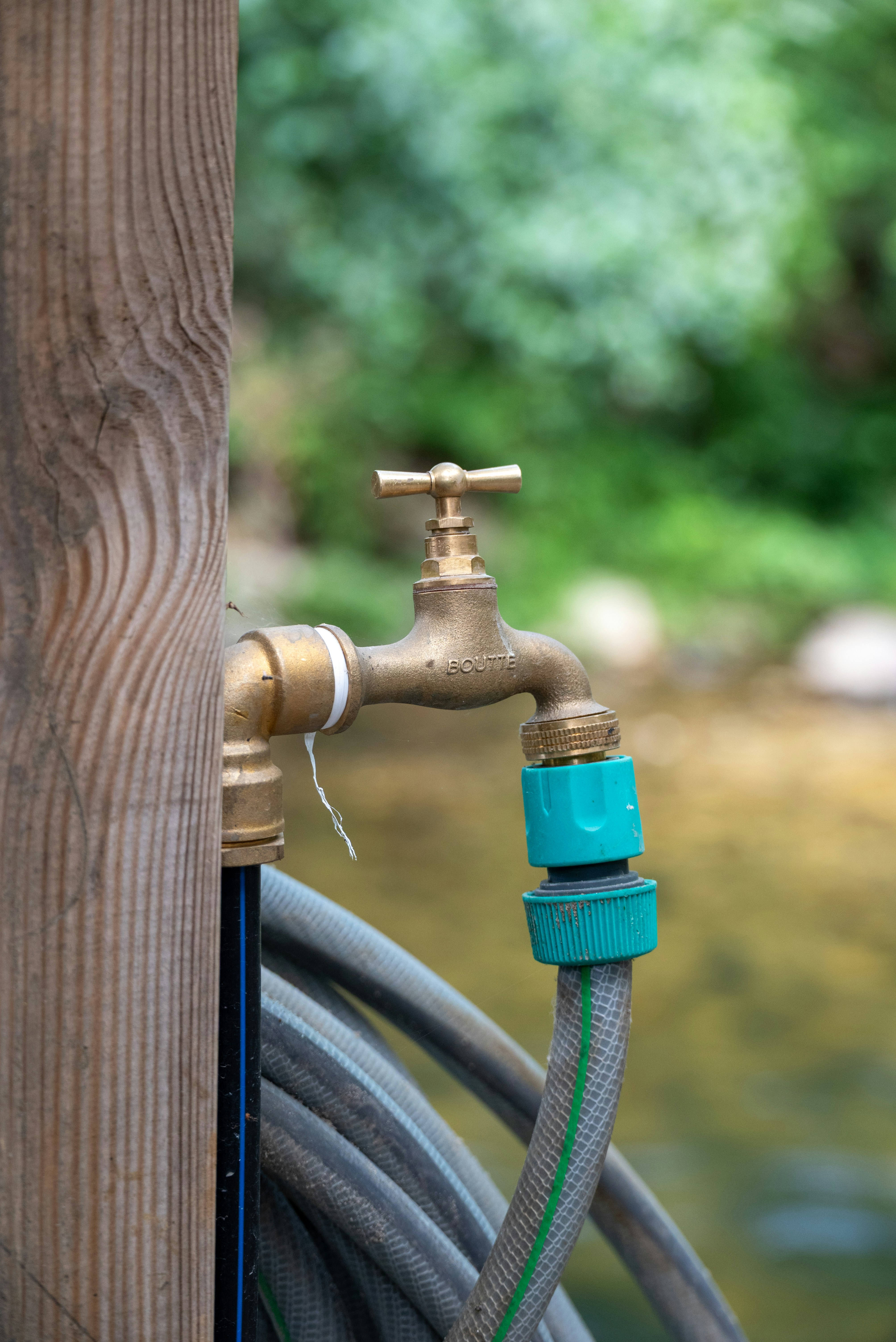 Brass outdoor faucet with green hose connector on a wooden post