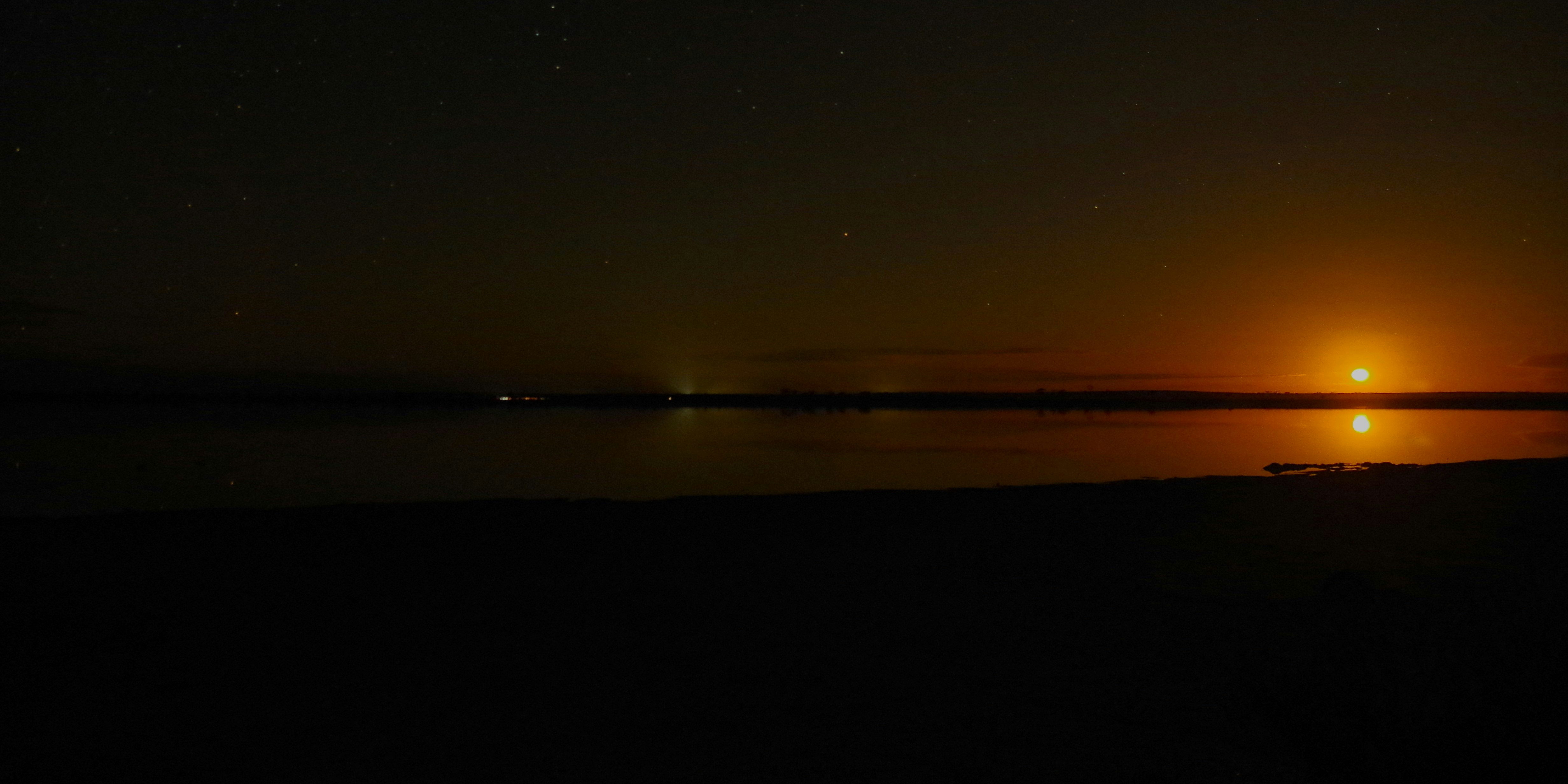 A bright orange moon glowing above a dark, still lake at night.