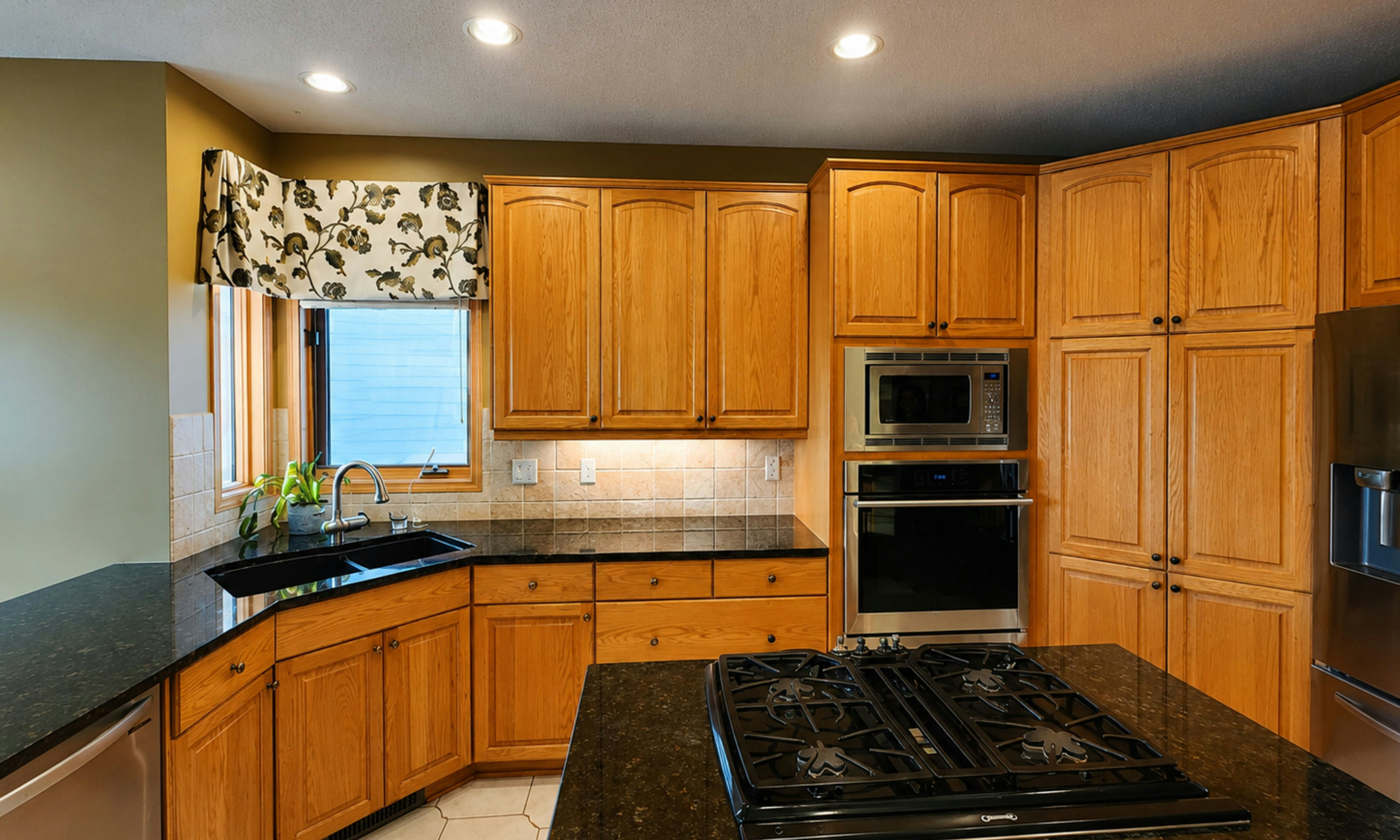 Dated kitchen with honey-oak cabinets and black countertops before renovation
