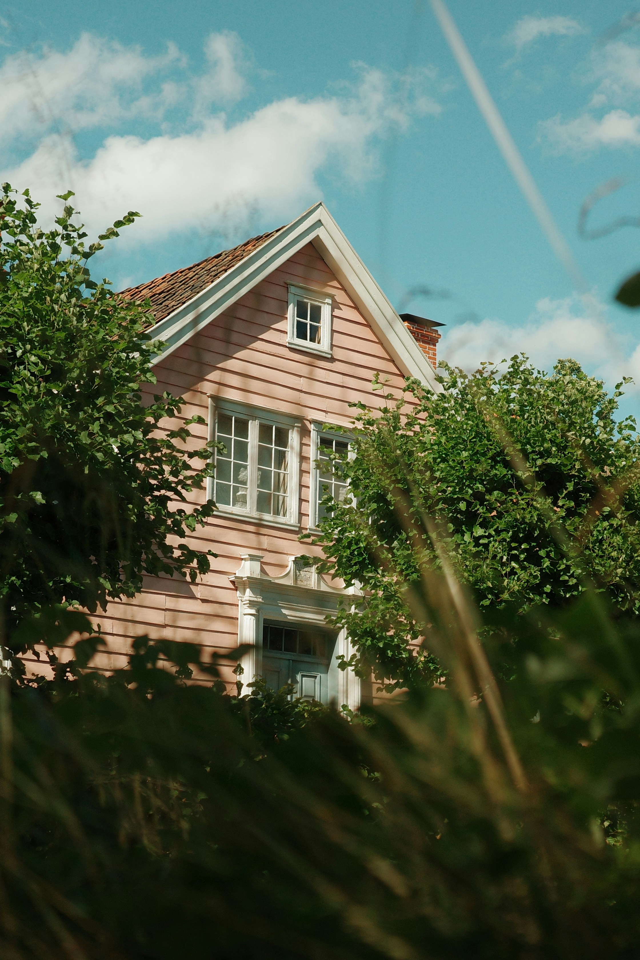 Ein rosa Holzhaus, eingerahmt von grünen Bäumen unter blauem Himmel