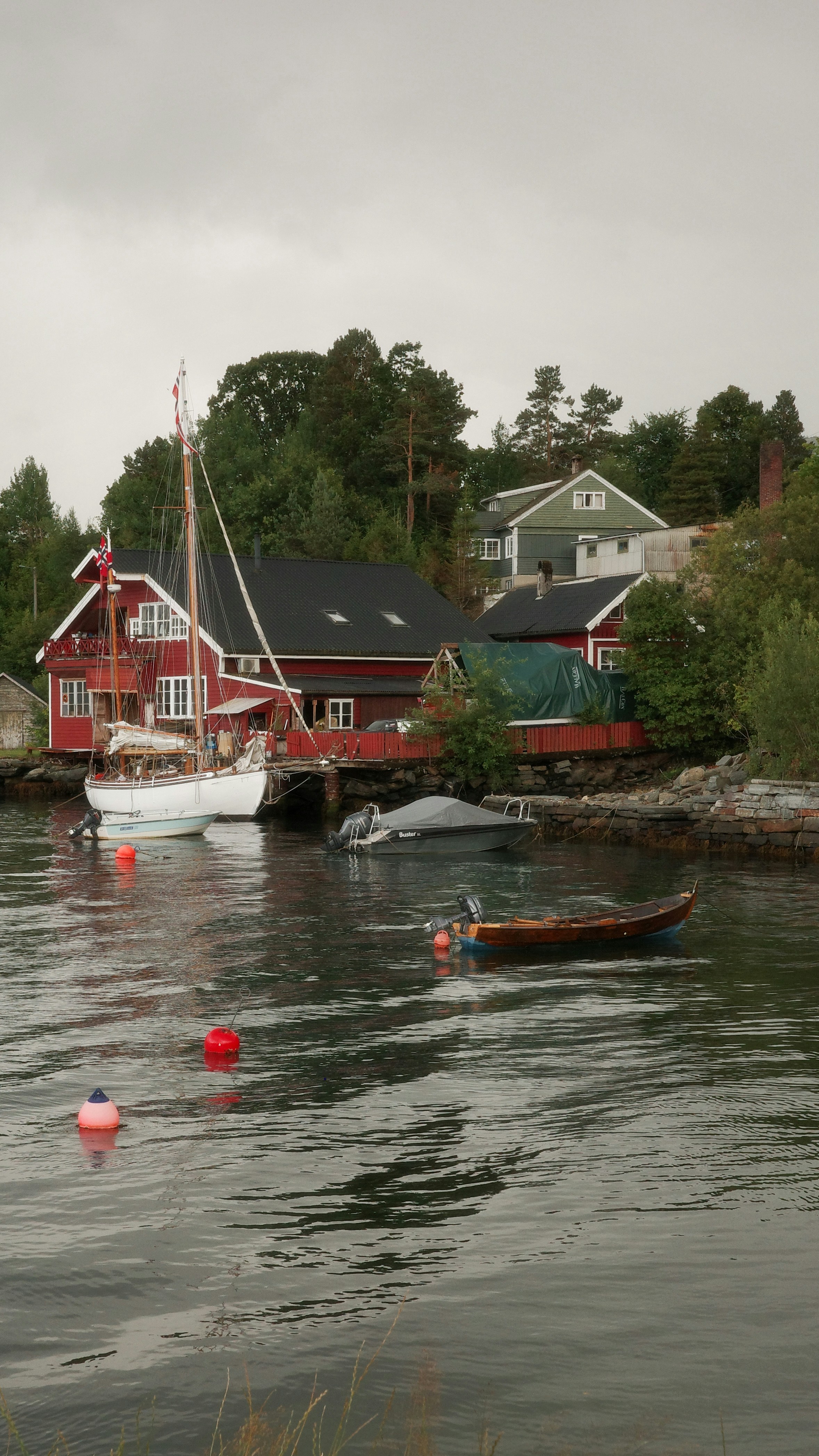 Ein Segelboot und kleine Motorboote lagen nahe roten Holzhäusern an einem felsigen Ufer