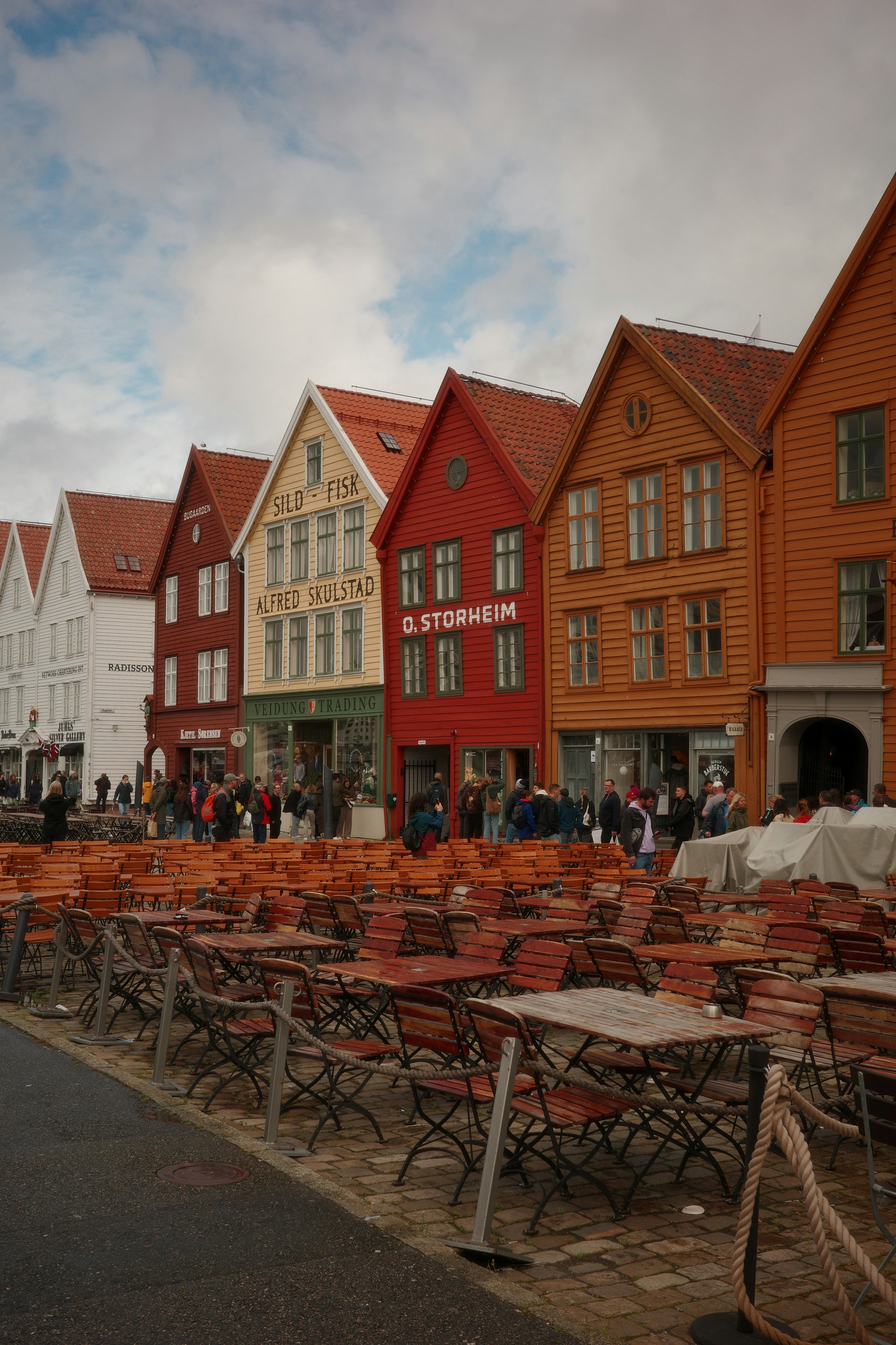 Holztische und -stühle vor bunten historischen Gebäuden in Bergen, Norwegen