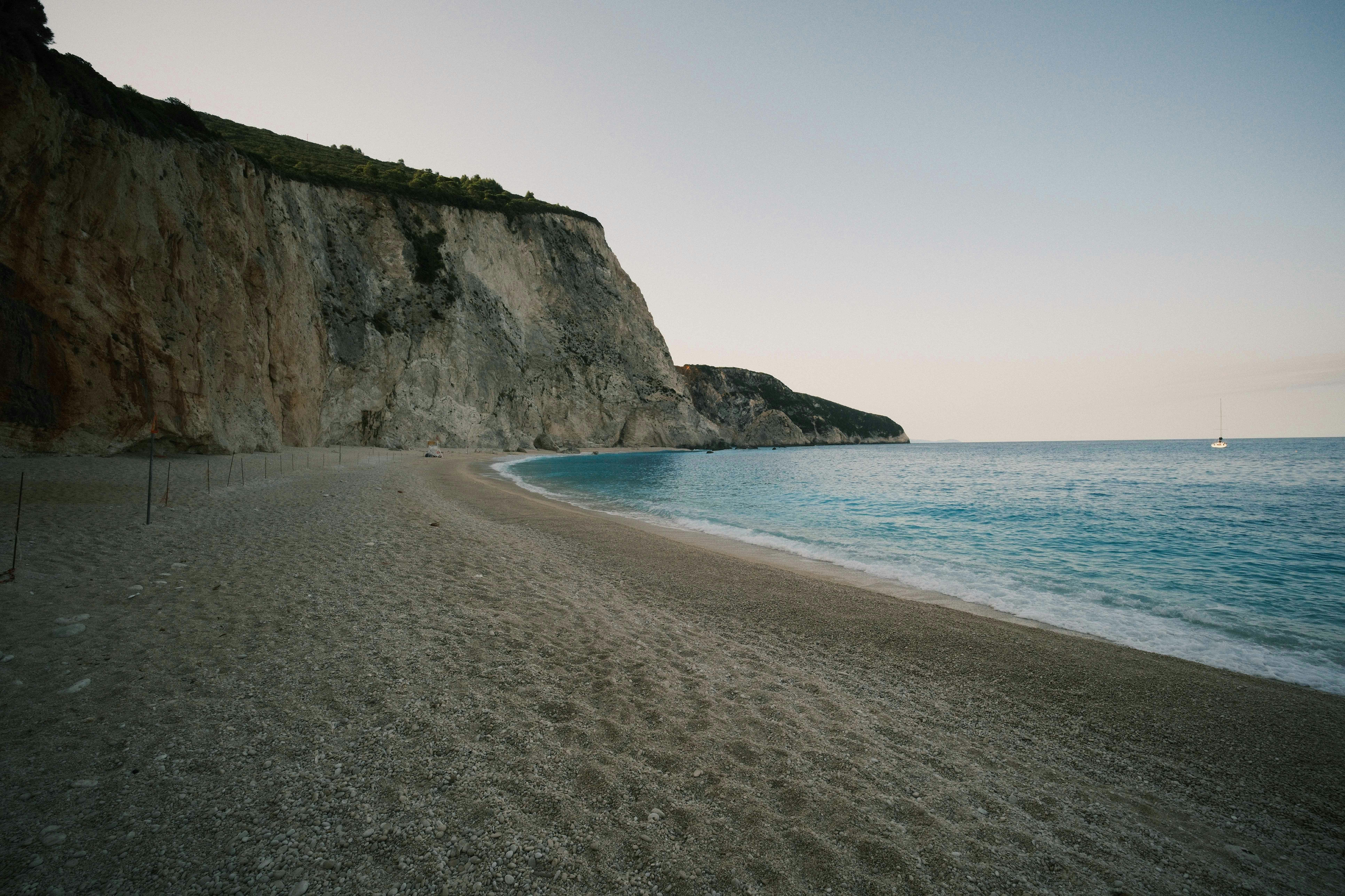 A pebble beach beneath a tall limestone cliff beside turquoise water