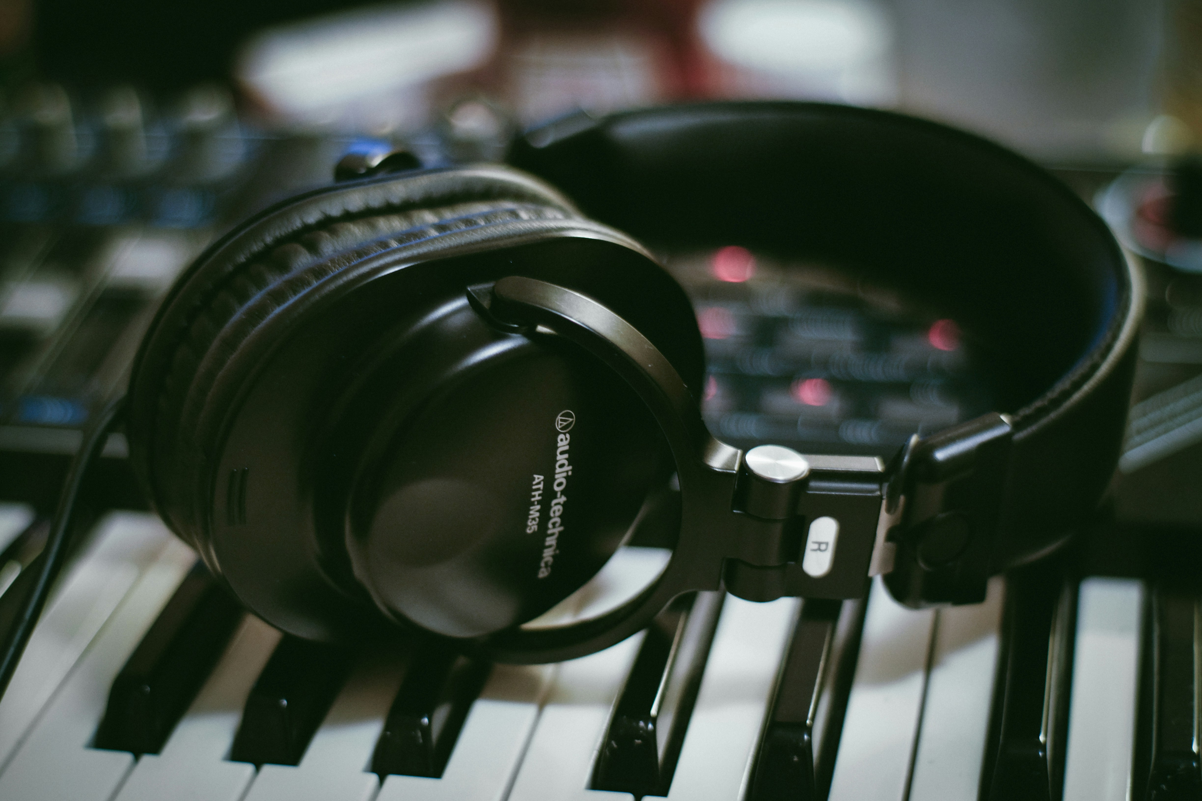 Black headphones resting on a white and black piano keyboard in a studio.